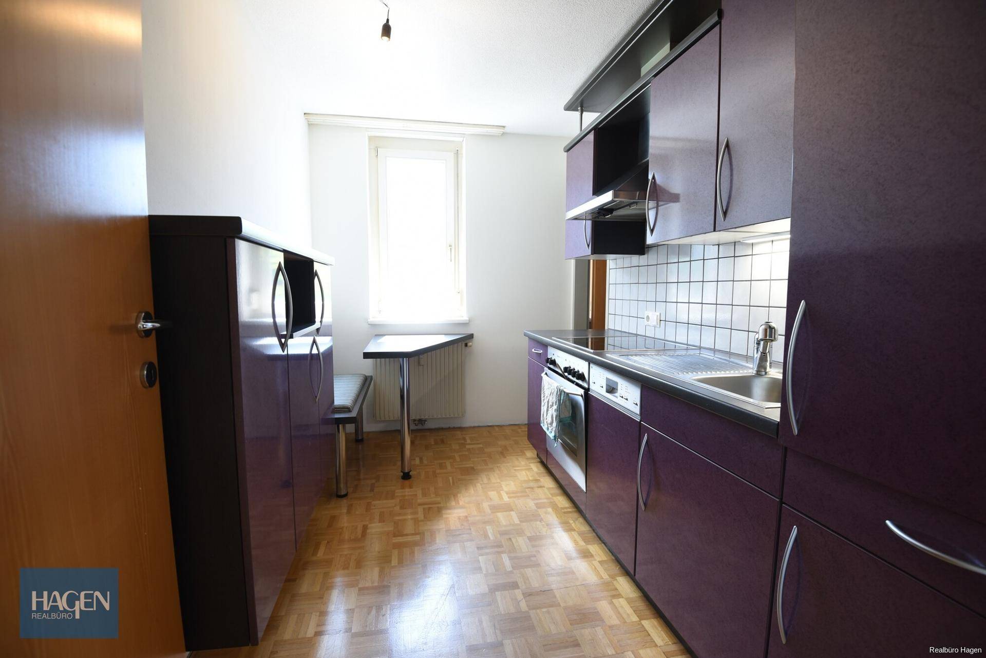 Kleine Küche mit lila Schränken, Fliesenrückwand und Fenster.