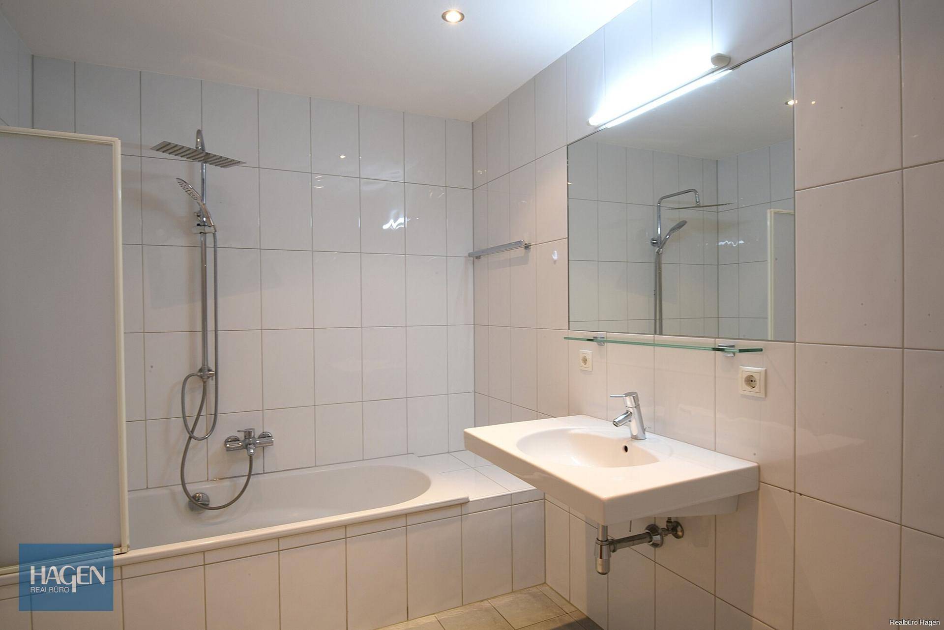 Helles Badezimmer mit Badewanne, Dusche und weiß gefliesten Wänden.
