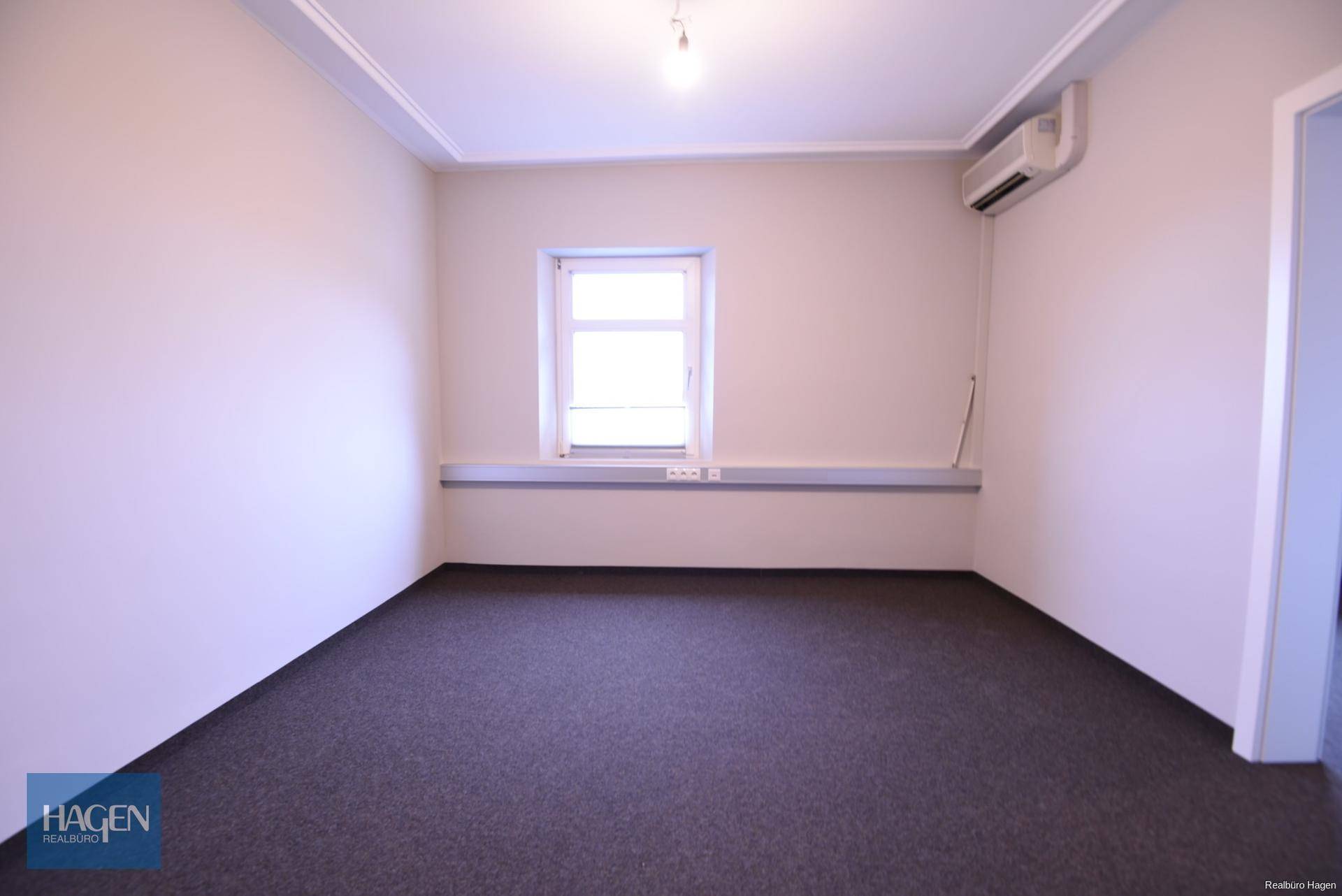 Leeres Büro mit hellem Fenster, Klimaanlage an der Wand montiert und dunklem Boden.