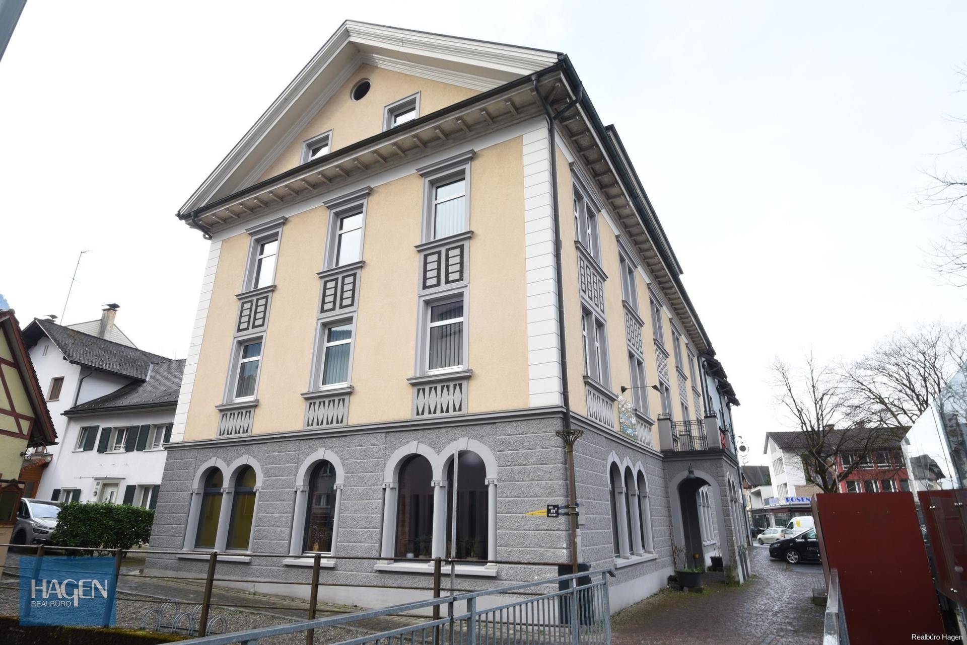 Historisches Gebäude mit gelber Fassade, grauer Steinfassade und traditioneller Architektur in städtischer Umgebung.