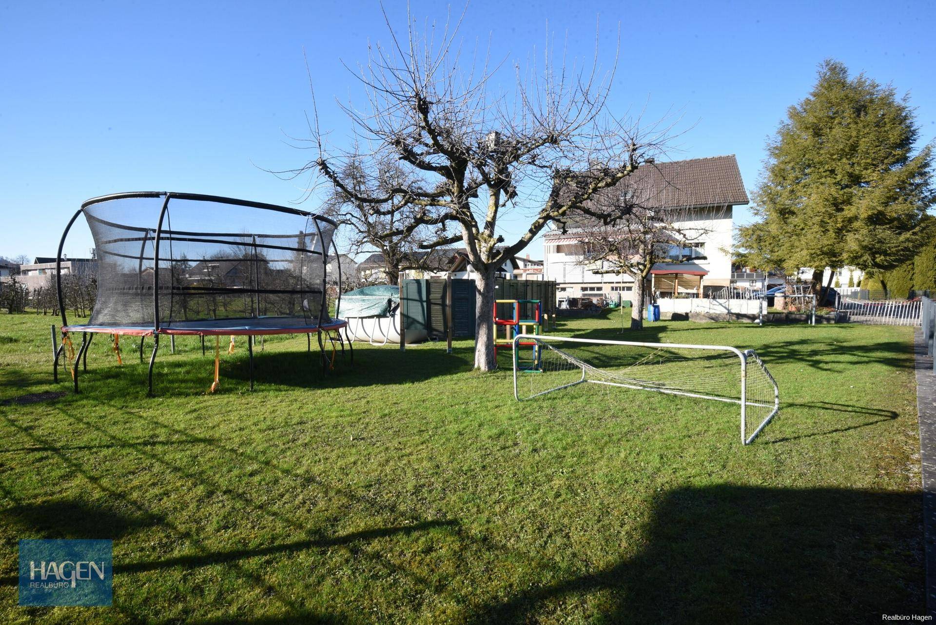 Weitläufiger Garten mit Rasenfläche, Trampolin und Fußballtor für Kinder.