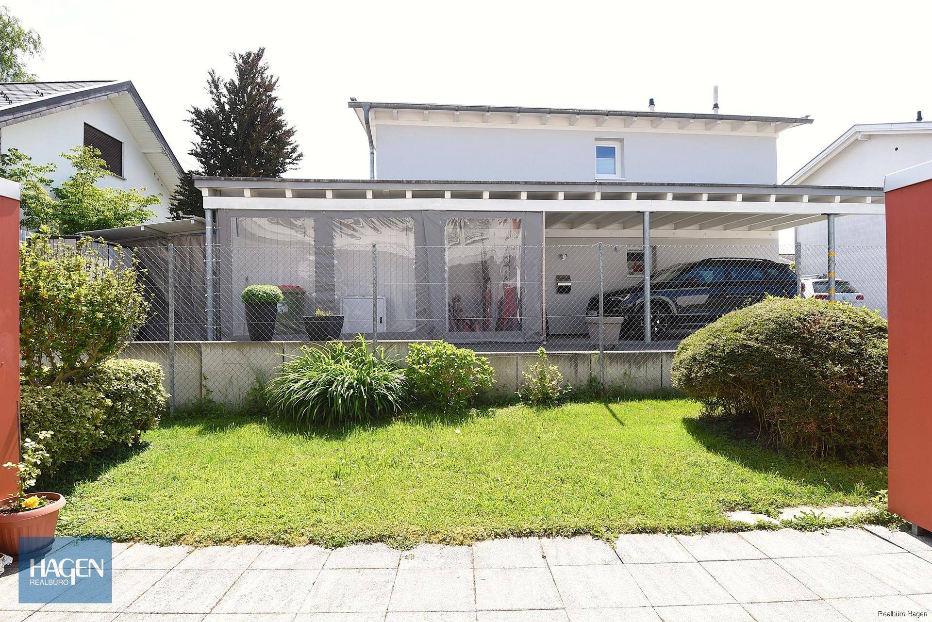 Vorderansicht des Hauses mit kleinem Vorgarten, gepflastertem Bereich und einem Carport.