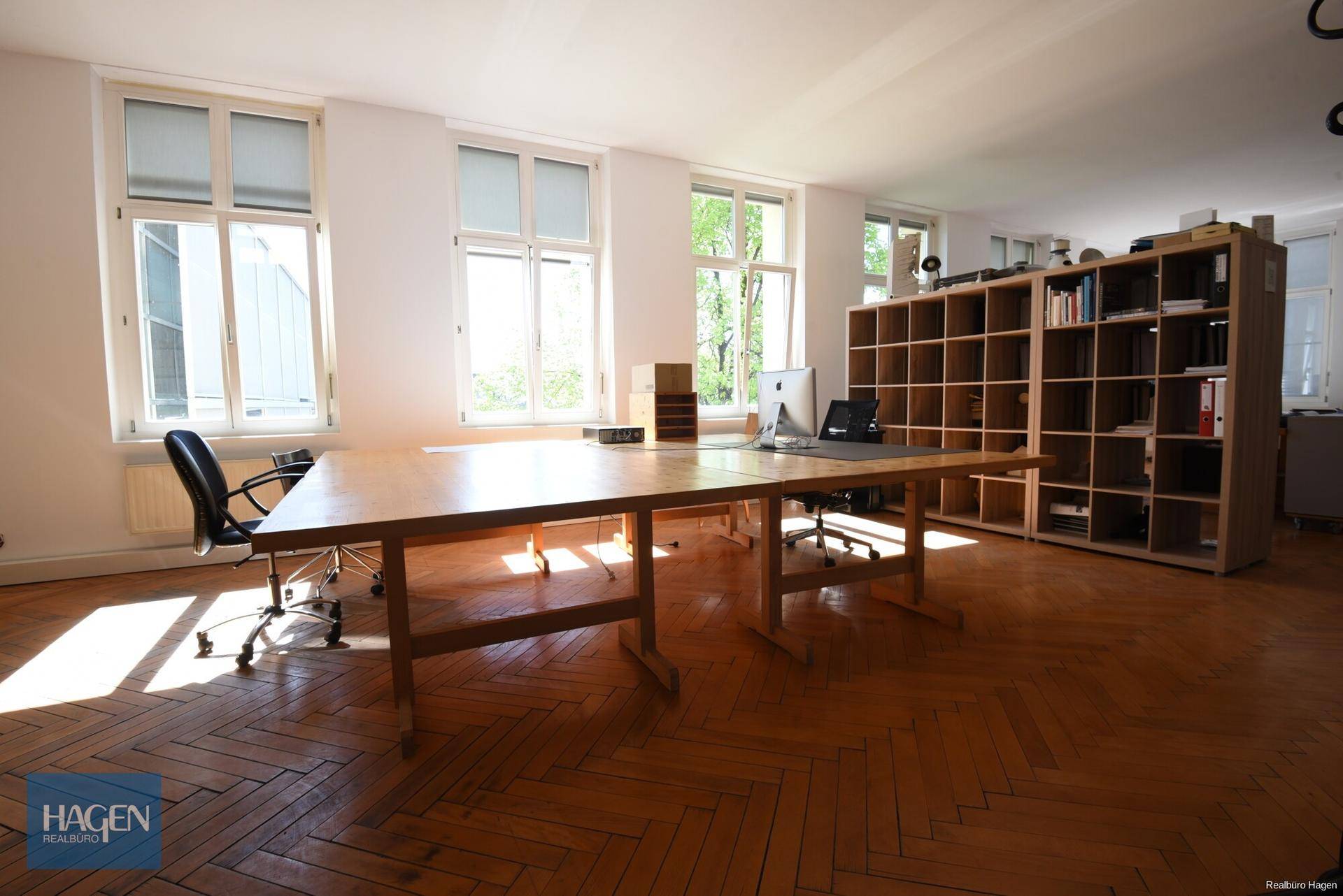 Geräumiges Büro mit Fischgrätparkett, großen Fenstern und viel natürlichem Licht, ausgestattet mit Schreibtischen.