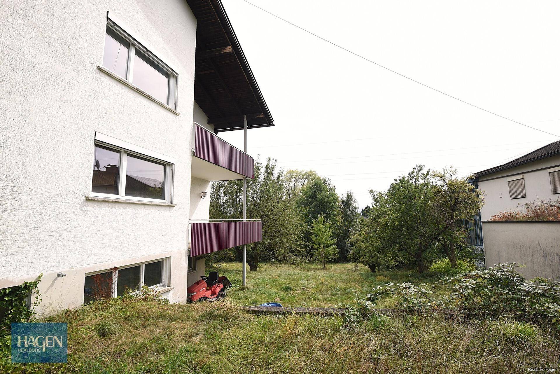 Seitenansicht des Hauses mit Balkonen und Blick auf das umliegende, bewachsene Grundstück.