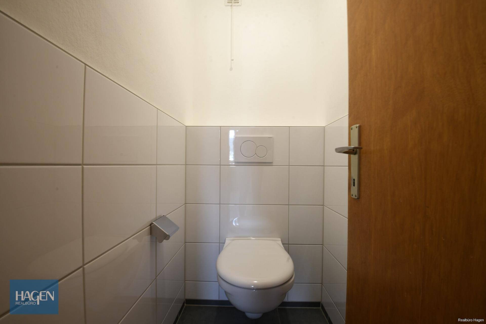 Separates WC mit Wand-WC und weißen Fliesen, funktional und sauber gestaltet.