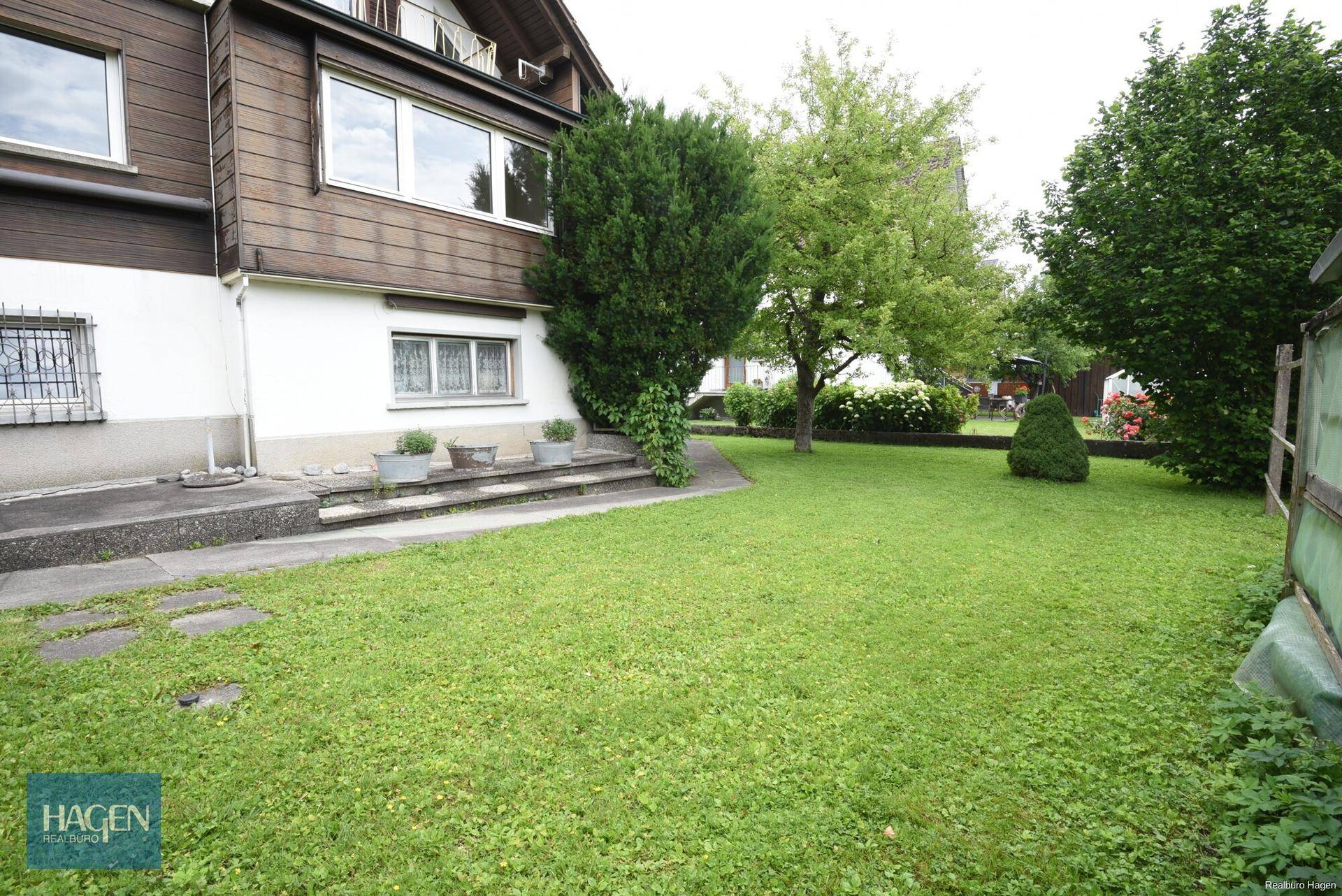 Gepflegter Garten mit Rasen, verschiedenen Bäumen und Sträuchern.