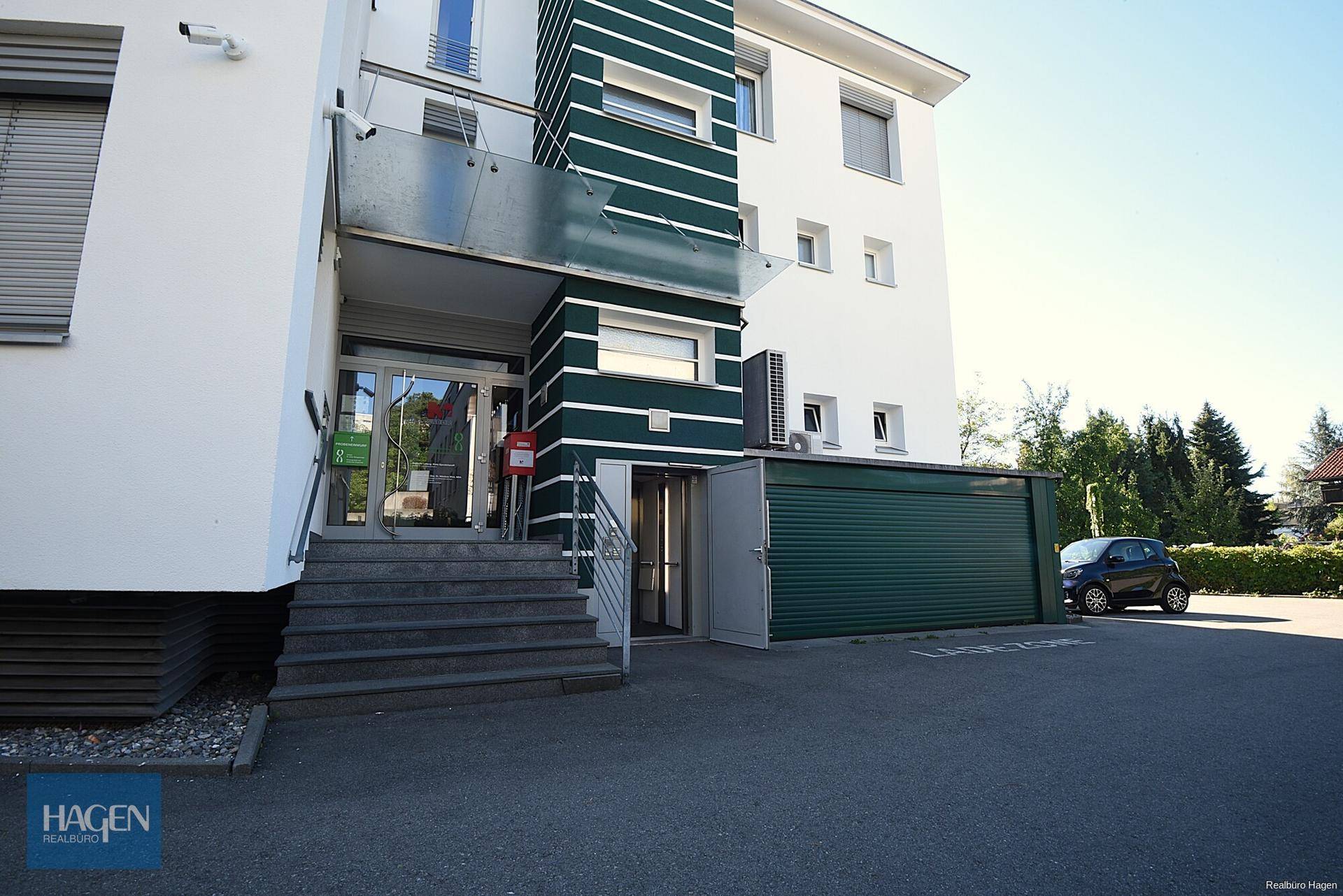 Gebäudeeingang mit Treppe, Rampe und einer grünen Garagentür an der Seite.