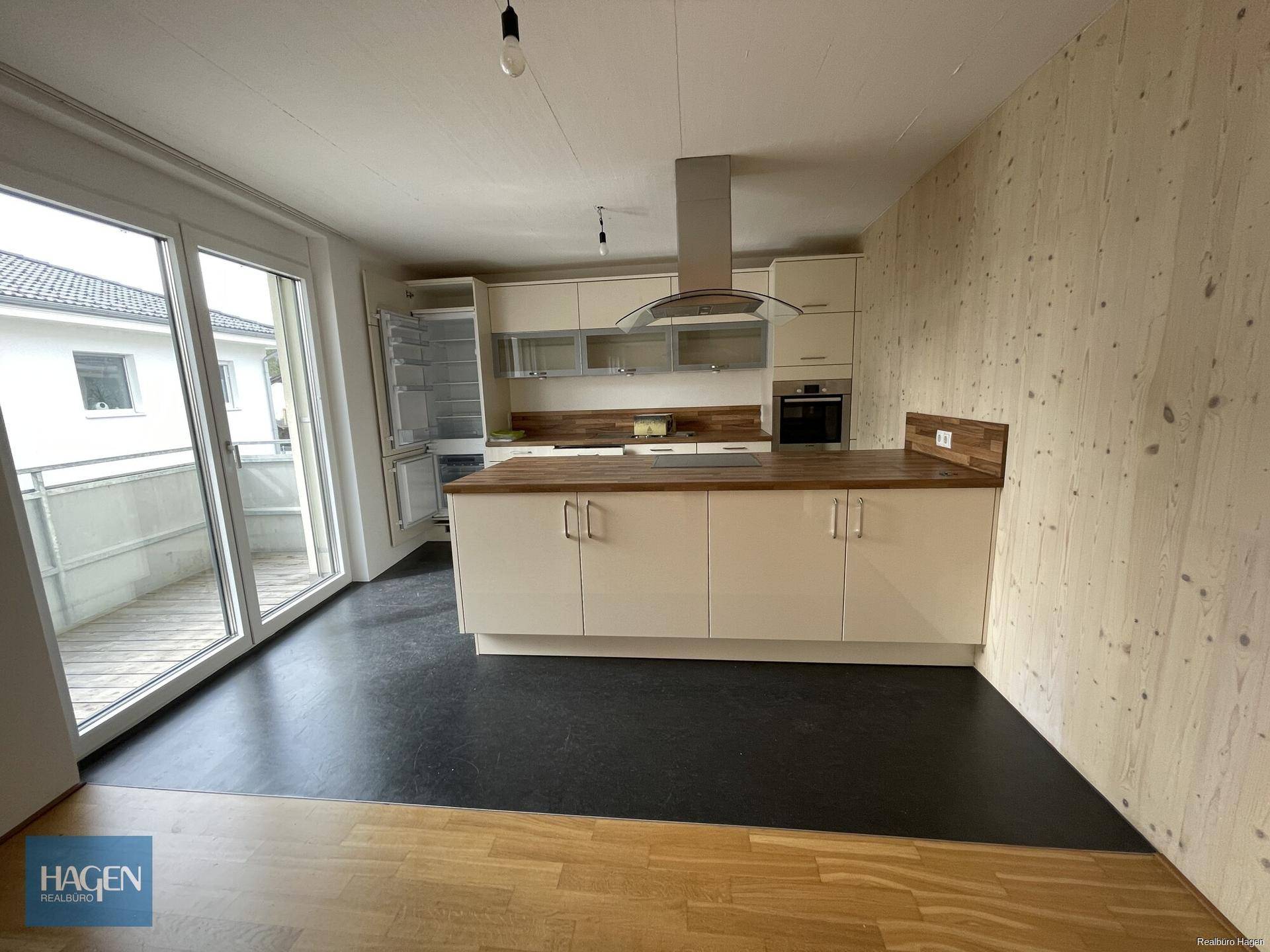 Moderne Einbauküche mit hellen Schränken, Holzarbeitsplatten und Zugang zu einem Balkon.