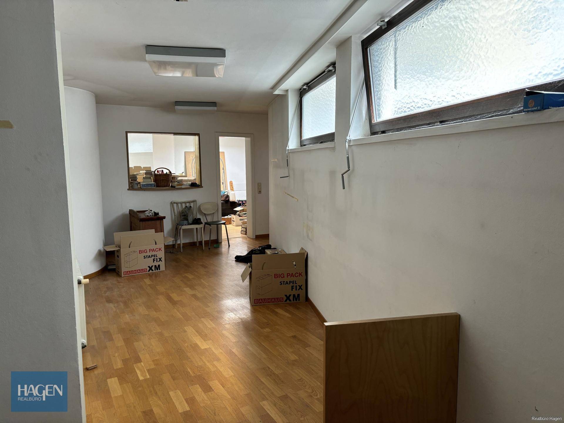 Geräumiger Raum mit Holzparkettboden und Fenstern, der als Lager oder Büro genutzt werden könnte.