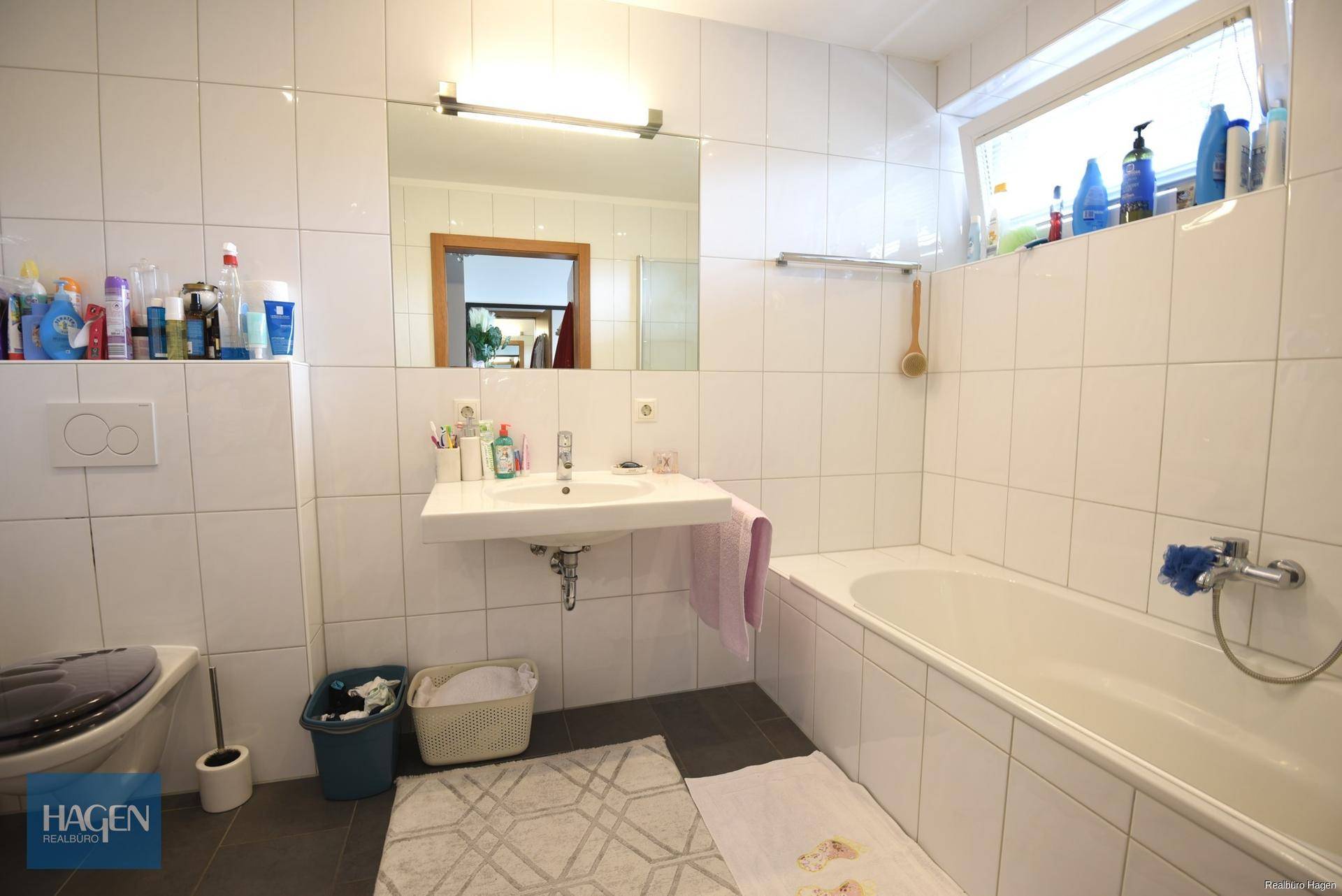 Modernes Badezimmer mit Badewanne, Waschbecken, Toilette und Fenster für natürliche Belüftung.