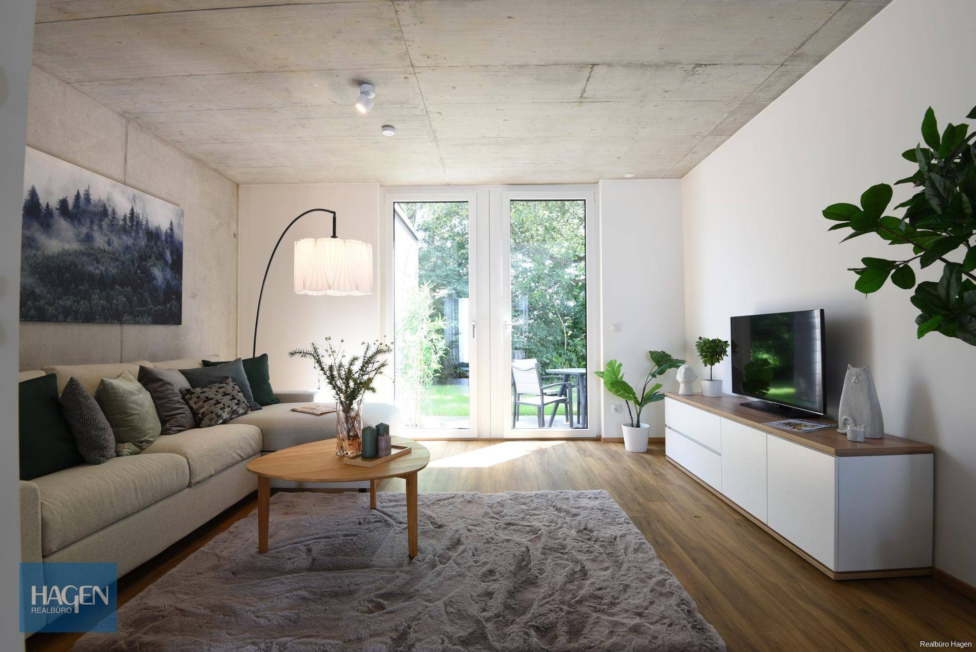 Helles Wohnzimmer mit beigem Sofa, Holzboden und großen Fenstern zum Garten.