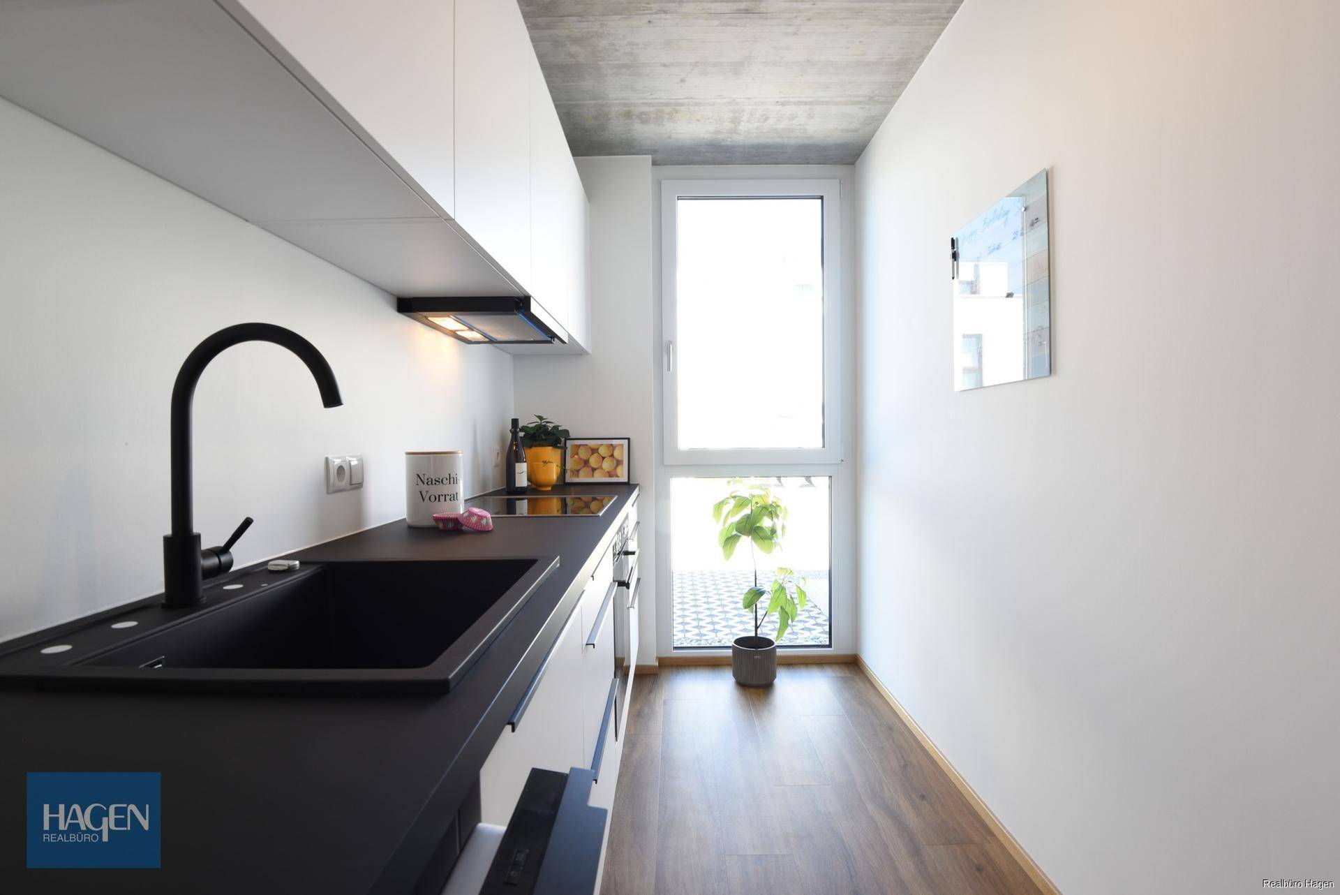 Moderne Küchenzeile mit schwarzer Spüle und Arbeitsplatte, Holzboden und Fenster.
