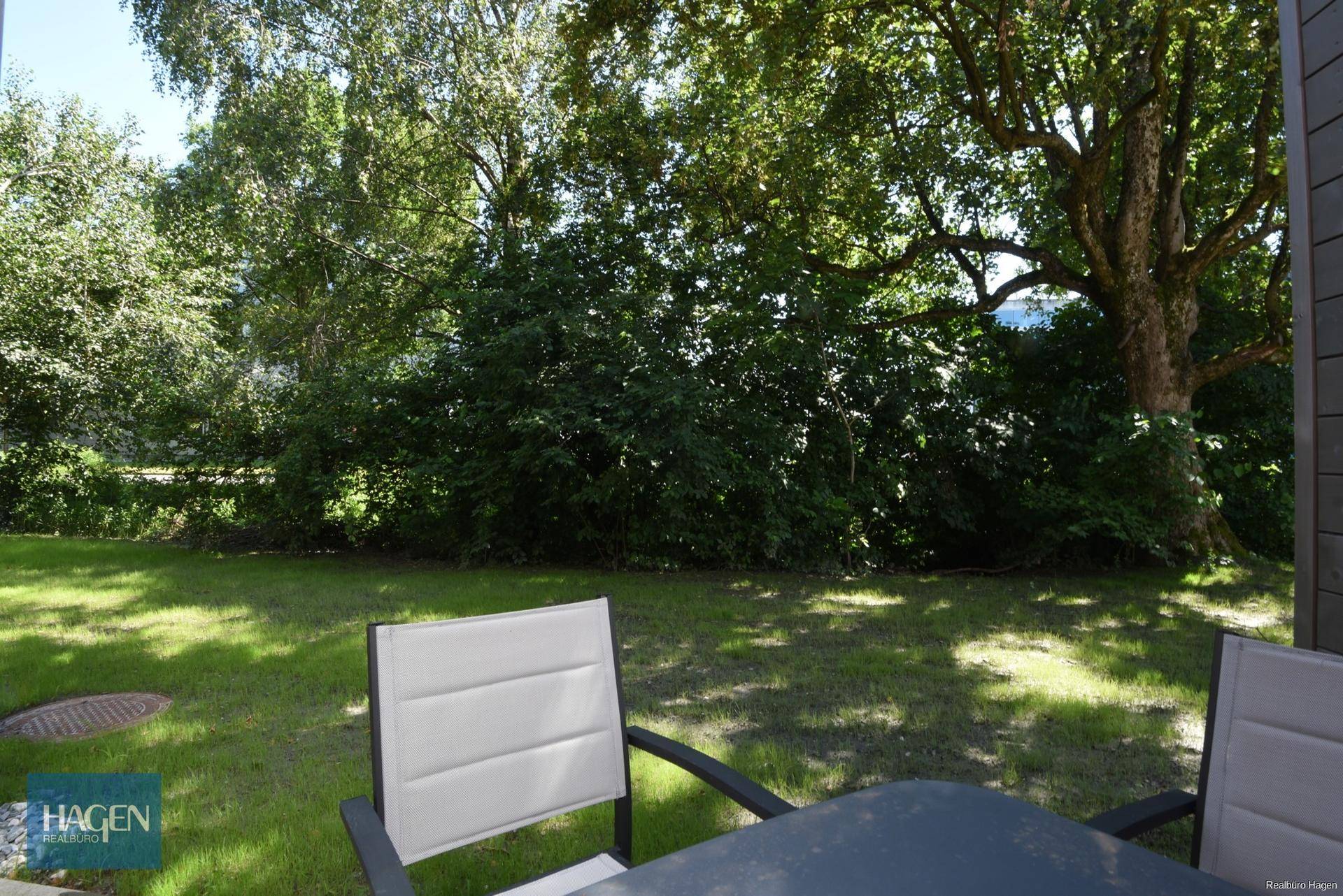 Grüne Rasenfläche mit Gartenmöbeln und üppiger Bepflanzung im Hintergrund.