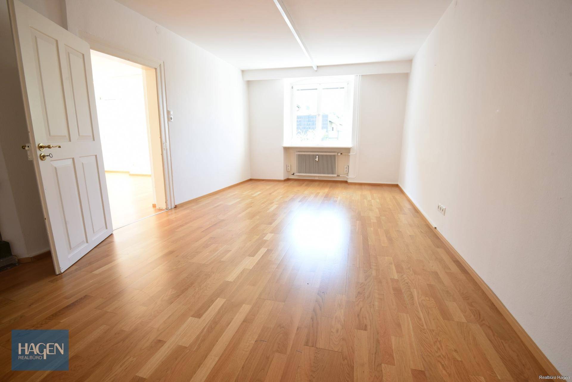 Helles Schlafzimmer mit Parkettboden und einem Fenster, das viel Tageslicht bietet.