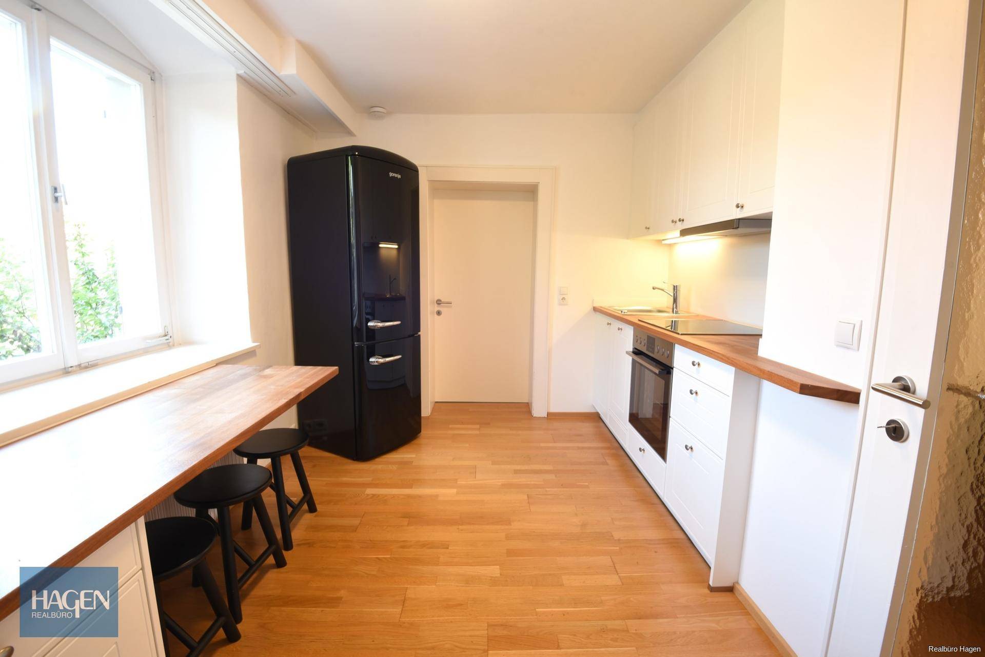 Funktionale Küche mit weißen Schränken, Holzarbeitsplatte und einem modernen schwarzen Kühlschrank.