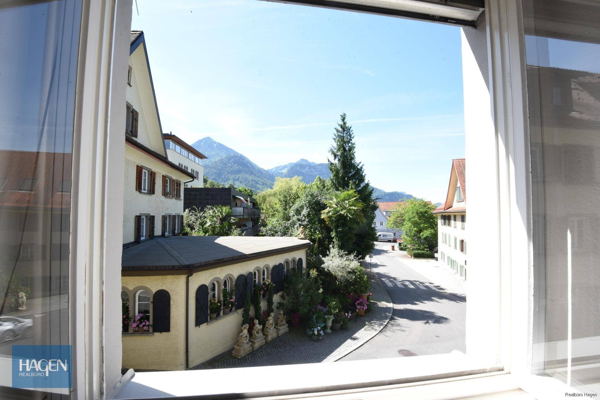 Panoramablick aus dem Fenster auf eine Straße, umliegende Gebäude und ferne Berge.