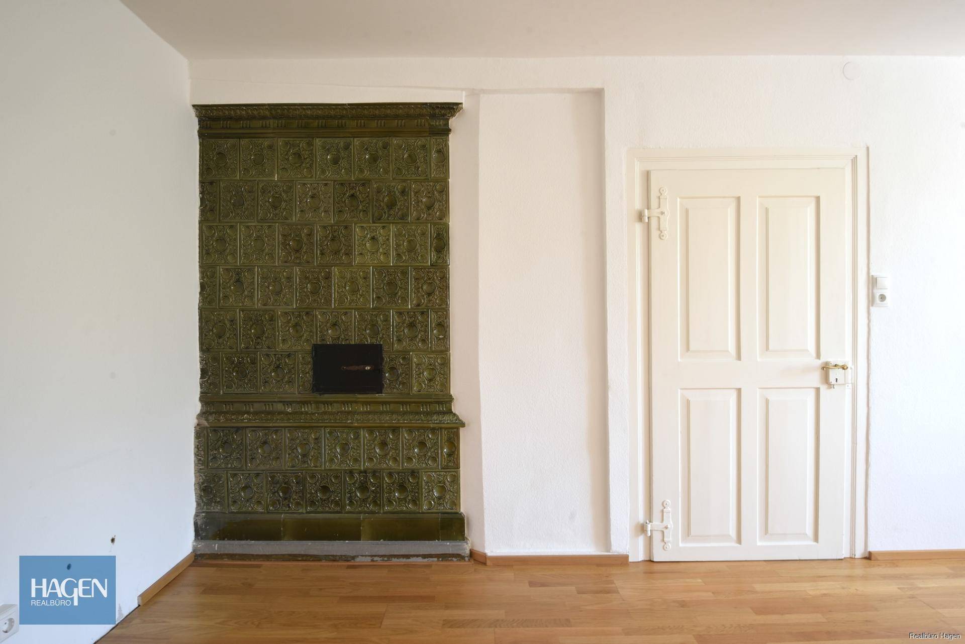 Detailansicht eines traditionellen grünen Kachelofens in einem hellen Wohnraum mit Parkettboden.