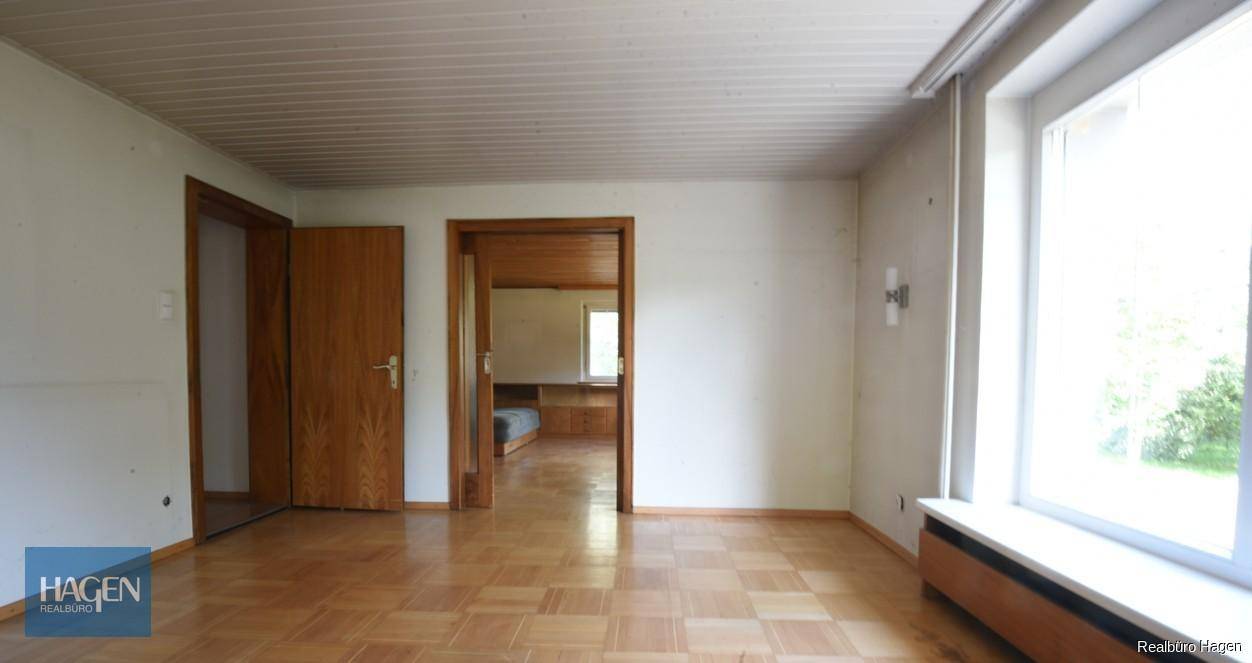 Helles Wohnzimmer mit Parkettboden, Holztüren und Blick ins Grüne durch große Fenster.