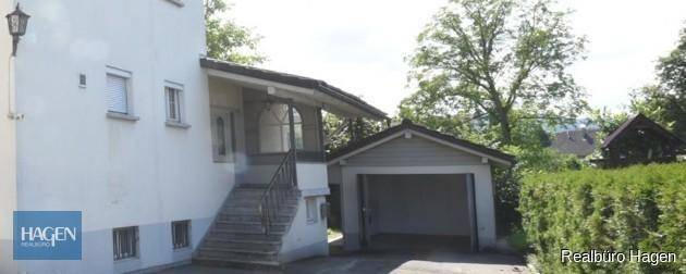 Hauseingang mit Treppe und angrenzender Garage, umgeben von gepflegter Hecke.