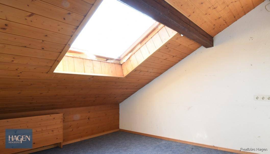 Dachzimmer mit Holzvertäfelung, Dachfenster und schrägen Wänden, bietet viel Licht.