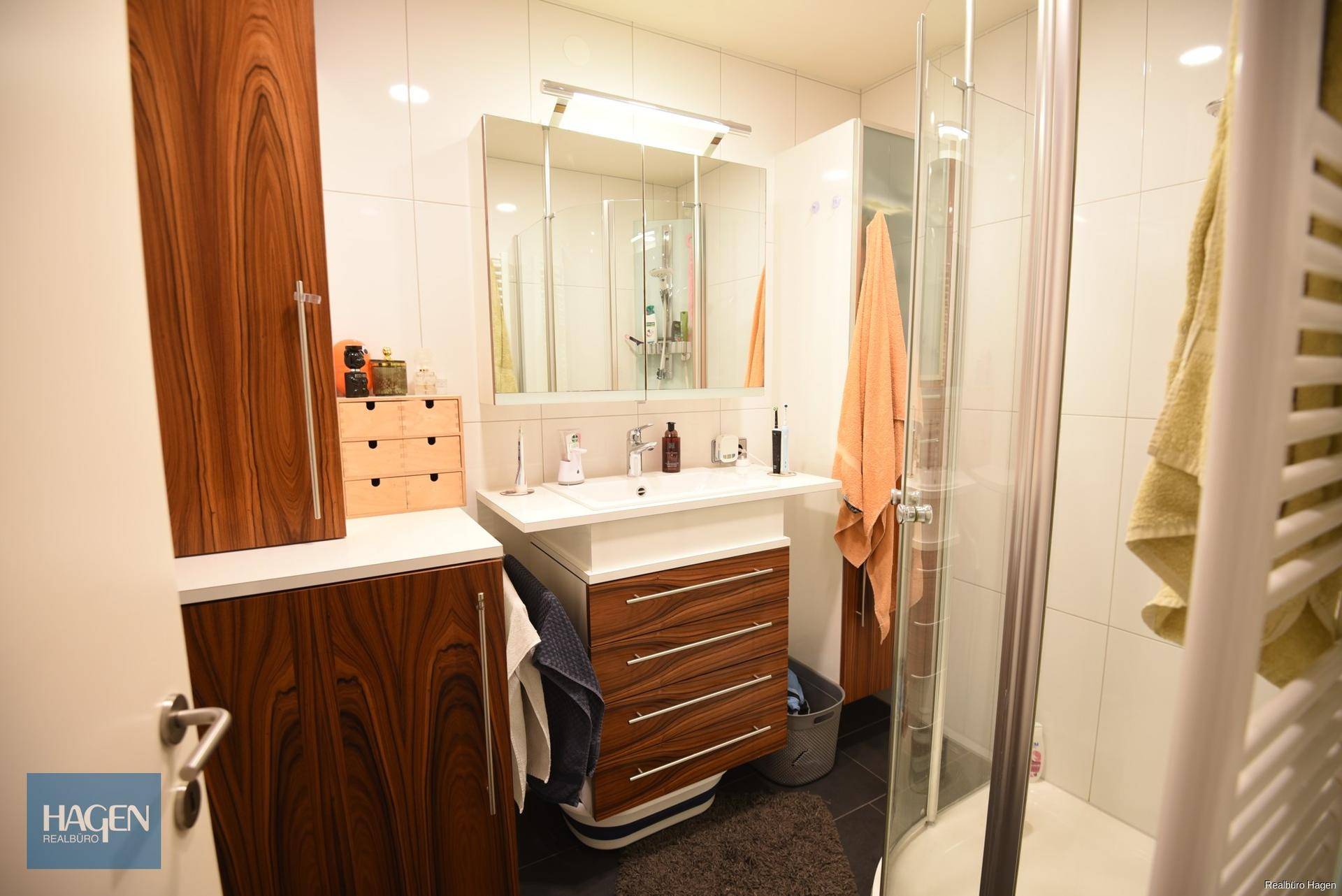 Modernes Badezimmer mit Dusche, Einzelwaschbecken und Holzmöbeln.