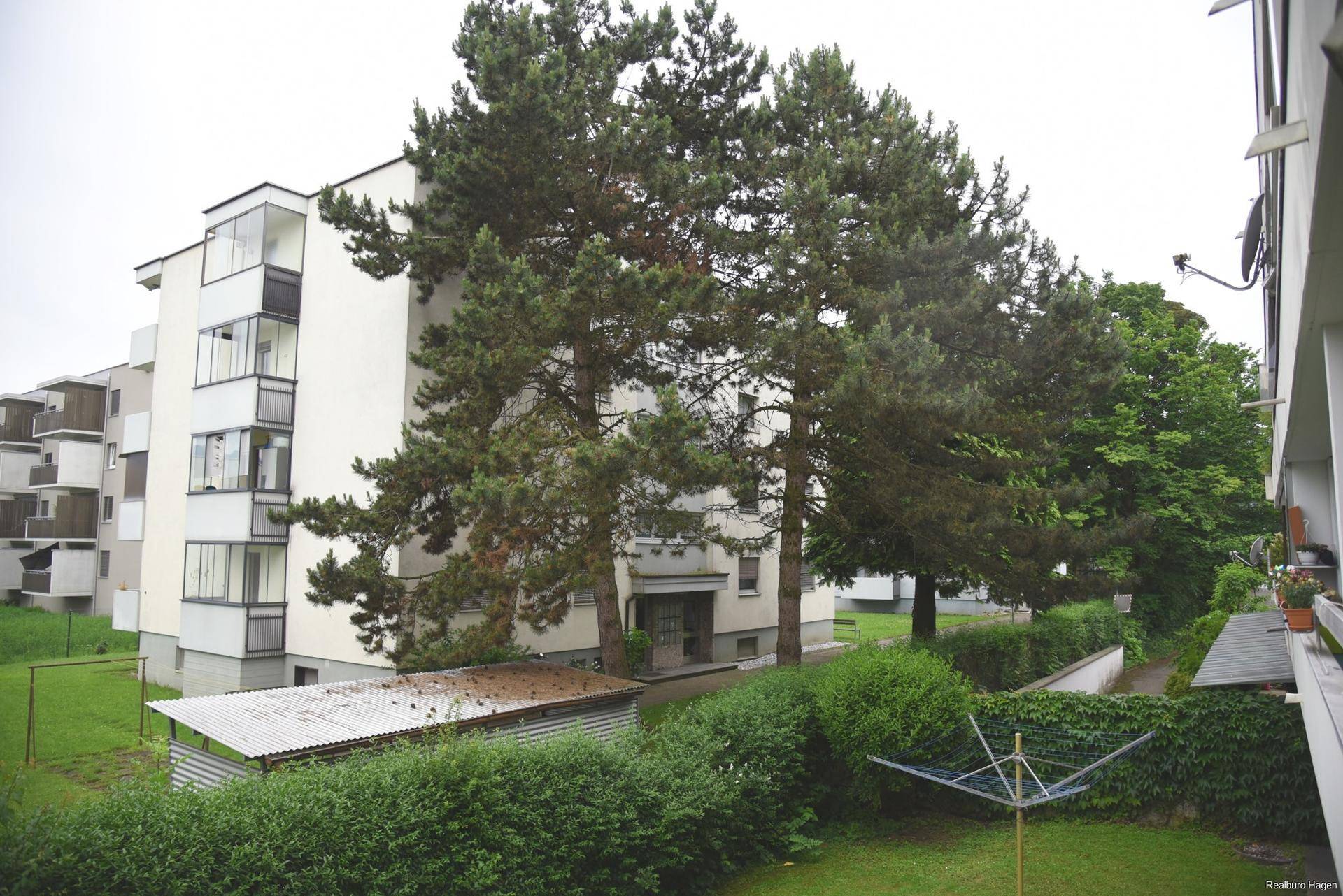 Mehrfamilienhaus mit Grünflächen und hohen Bäumen in der Umgebung.