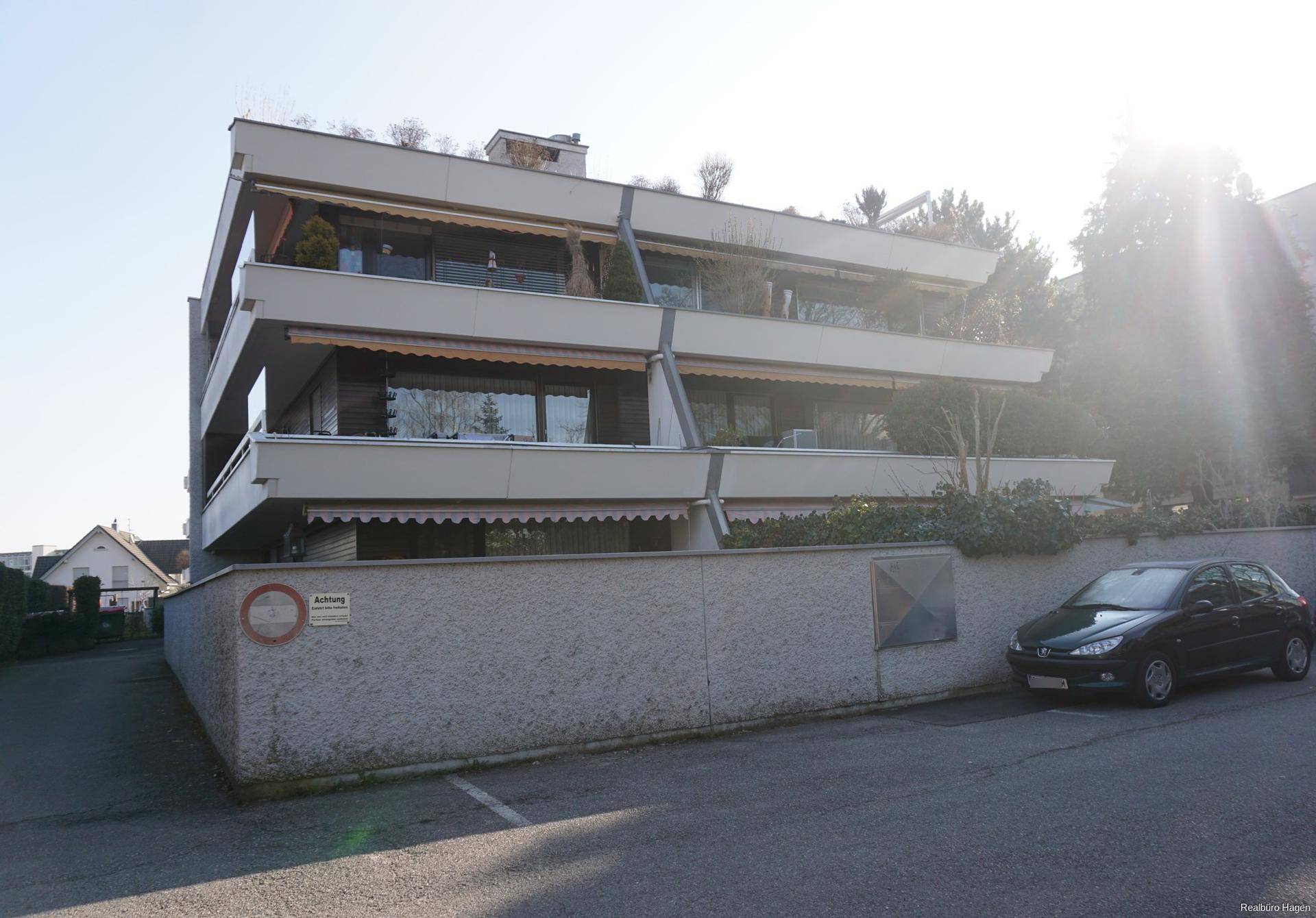 Mehrfamilienhaus mit mehreren Balkonen und Markisen an einem sonnigen Tag.