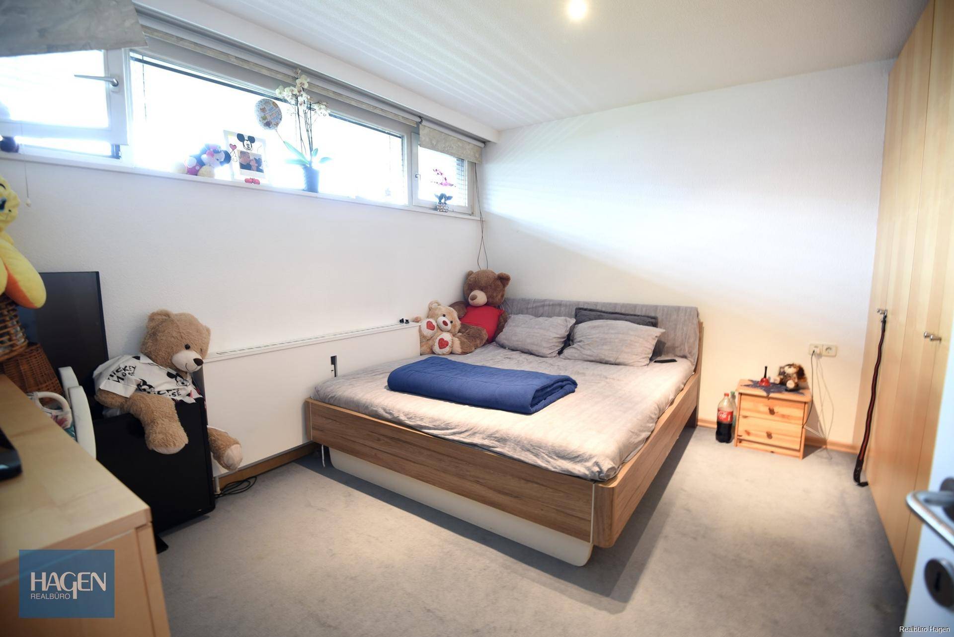 Schlafzimmer mit Teppichboden, großem Fenster und Holzschrank.