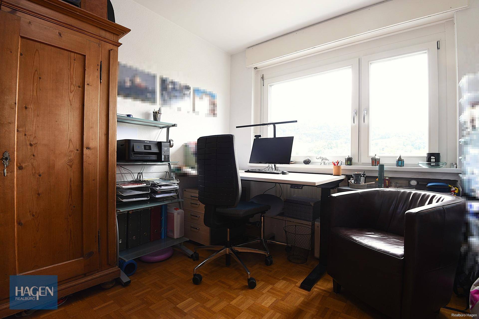 Helles Arbeitszimmer mit Schreibtisch, Bürostuhl und einem traditionellen Holzschrank.