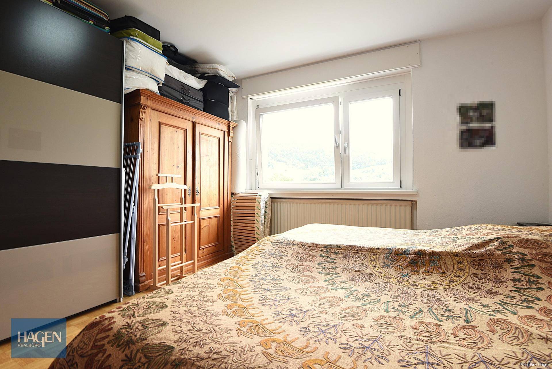 Schlafzimmer mit großem Bett, einem klassischen Holzschrank und einem Fenster.