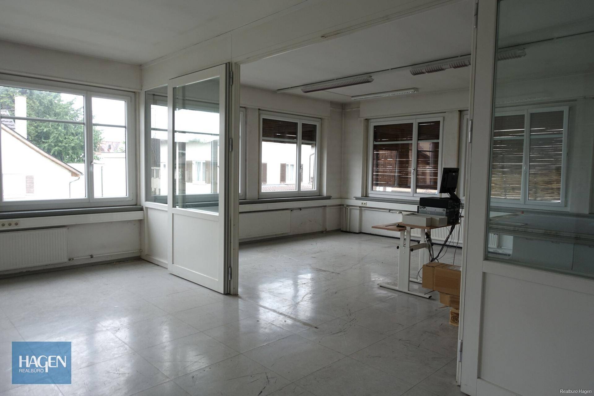Heller Büroraum mit großen Fenstern, Trennwänden aus Glas und Fliesenboden.