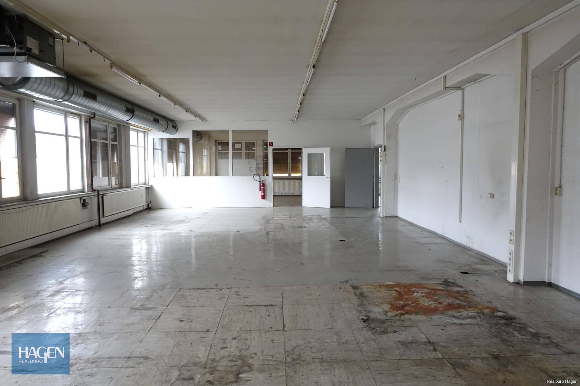Weitläufiger, leerer Industrieraum mit großen Fenstern und sichtbaren Lüftungsanlagen.