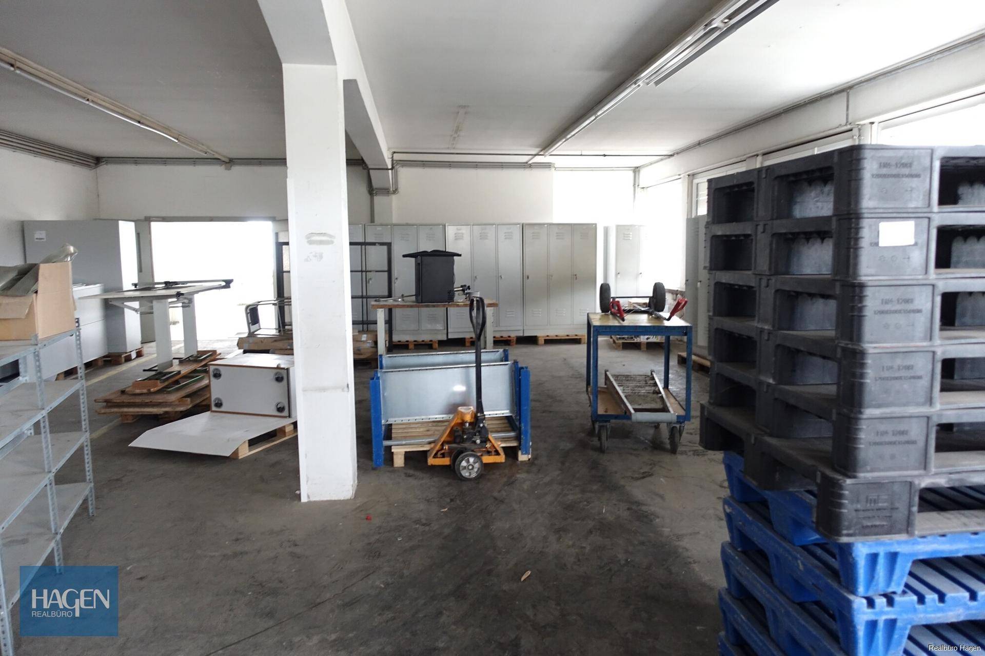 Werkstatt- oder Lagerbereich mit Regalen, Paletten und Arbeitsgeräten.