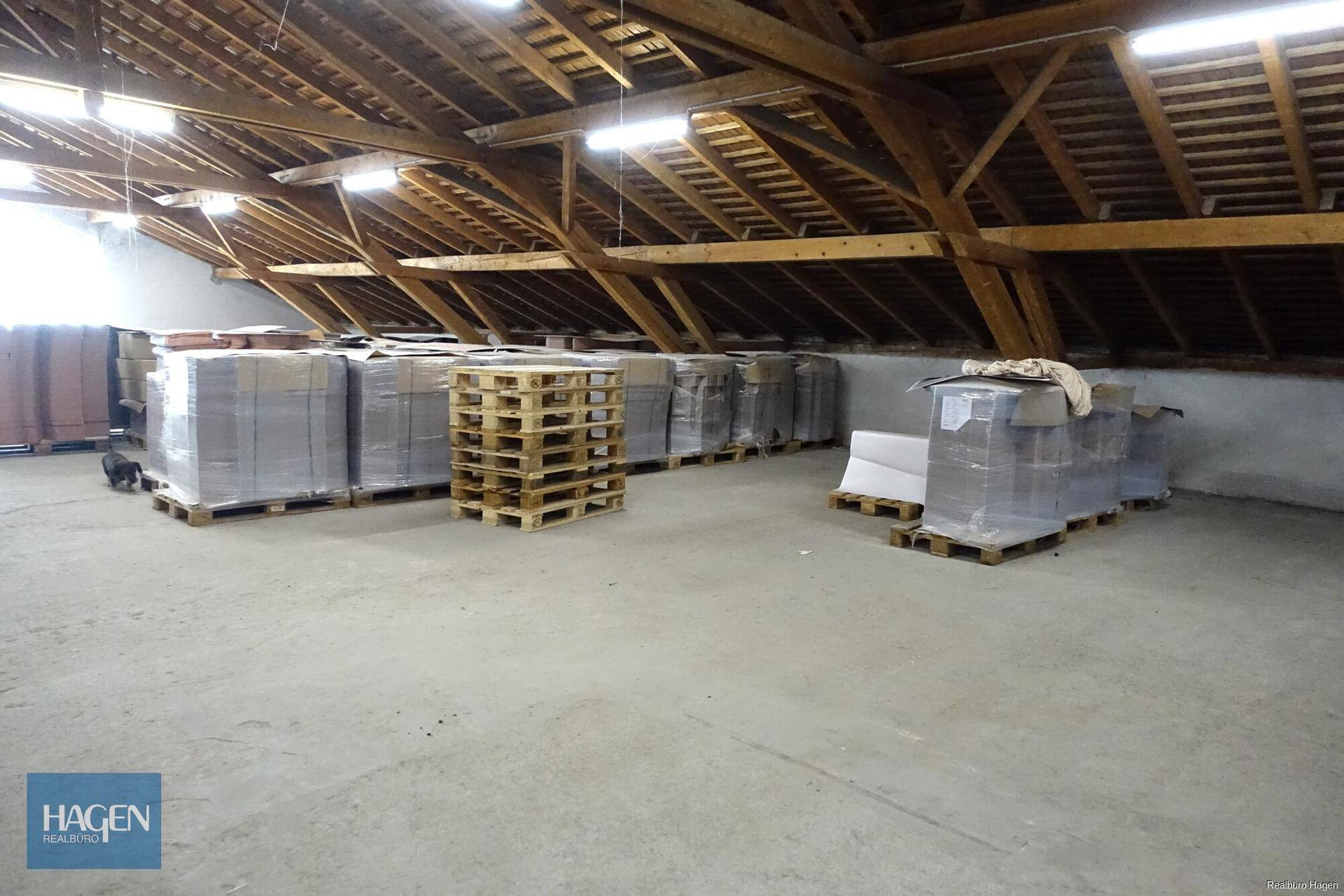Weitläufiger Dachboden mit Holzdachstuhl, genutzt als Lagerfläche für verpackte Waren.