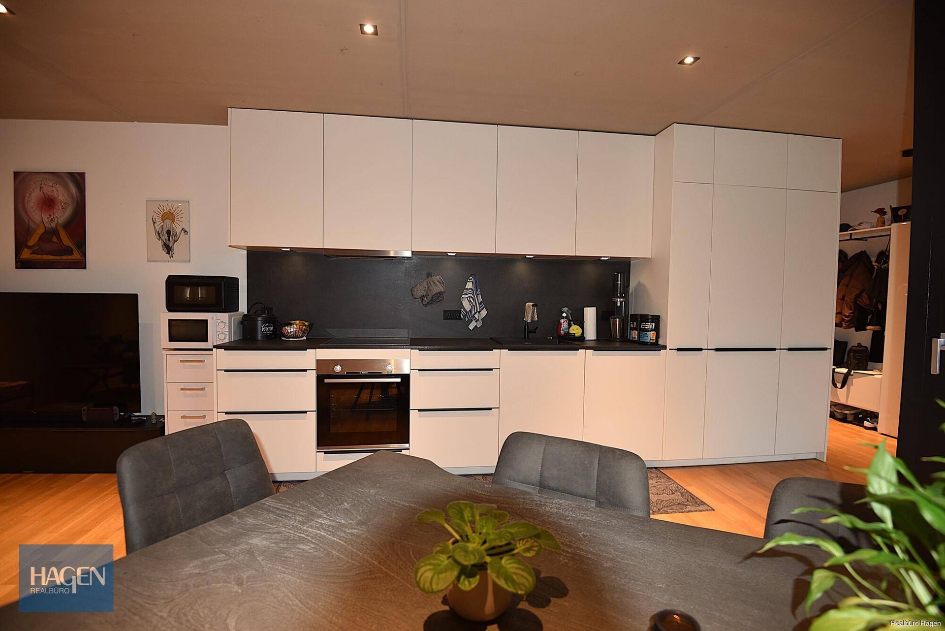 Moderne Einbauküche mit weißen Schränken, dunkler Arbeitsplatte und integrierten Geräten.