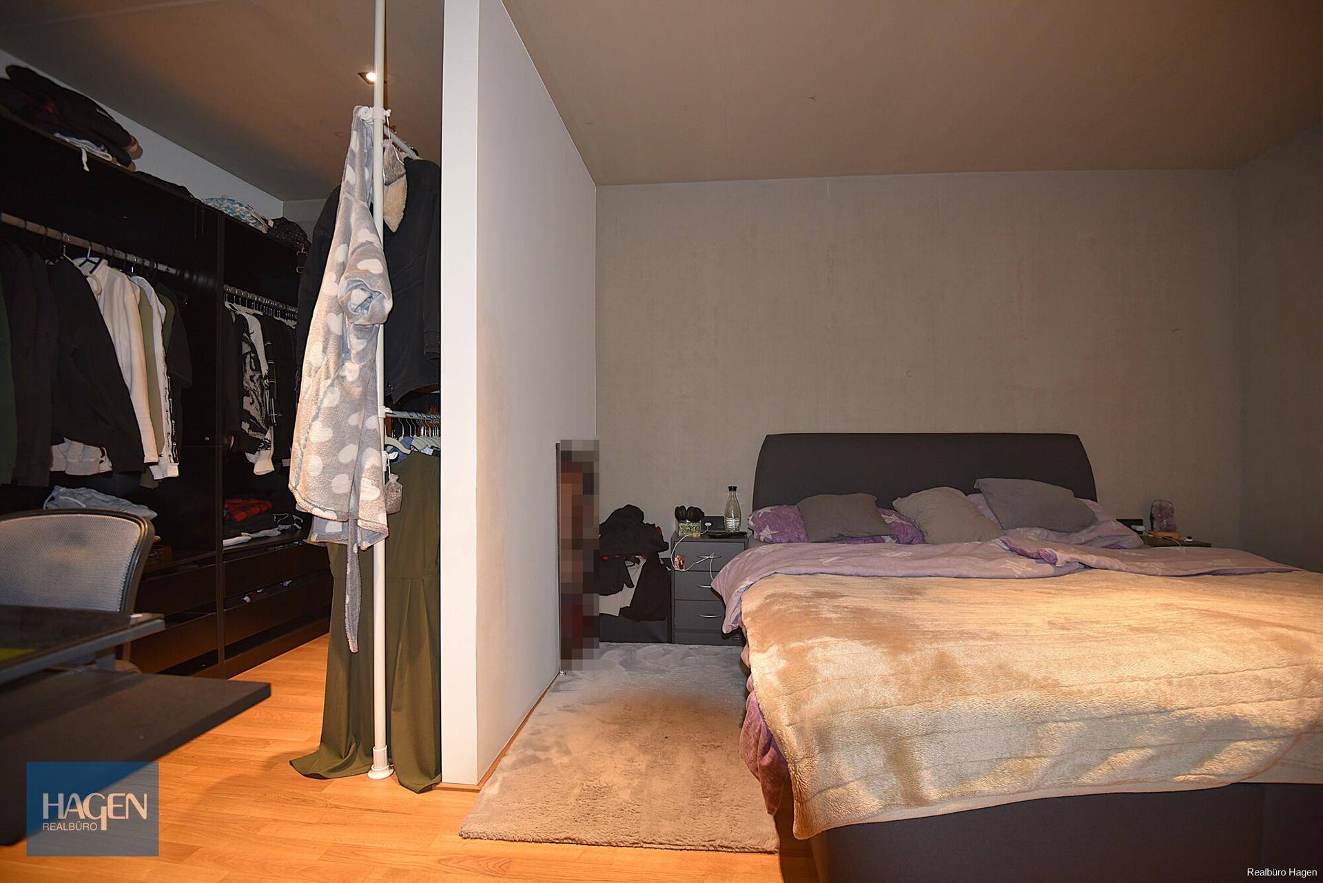 Schlafzimmer mit Doppelbett und offenem Kleiderschrankbereich auf Holzboden.