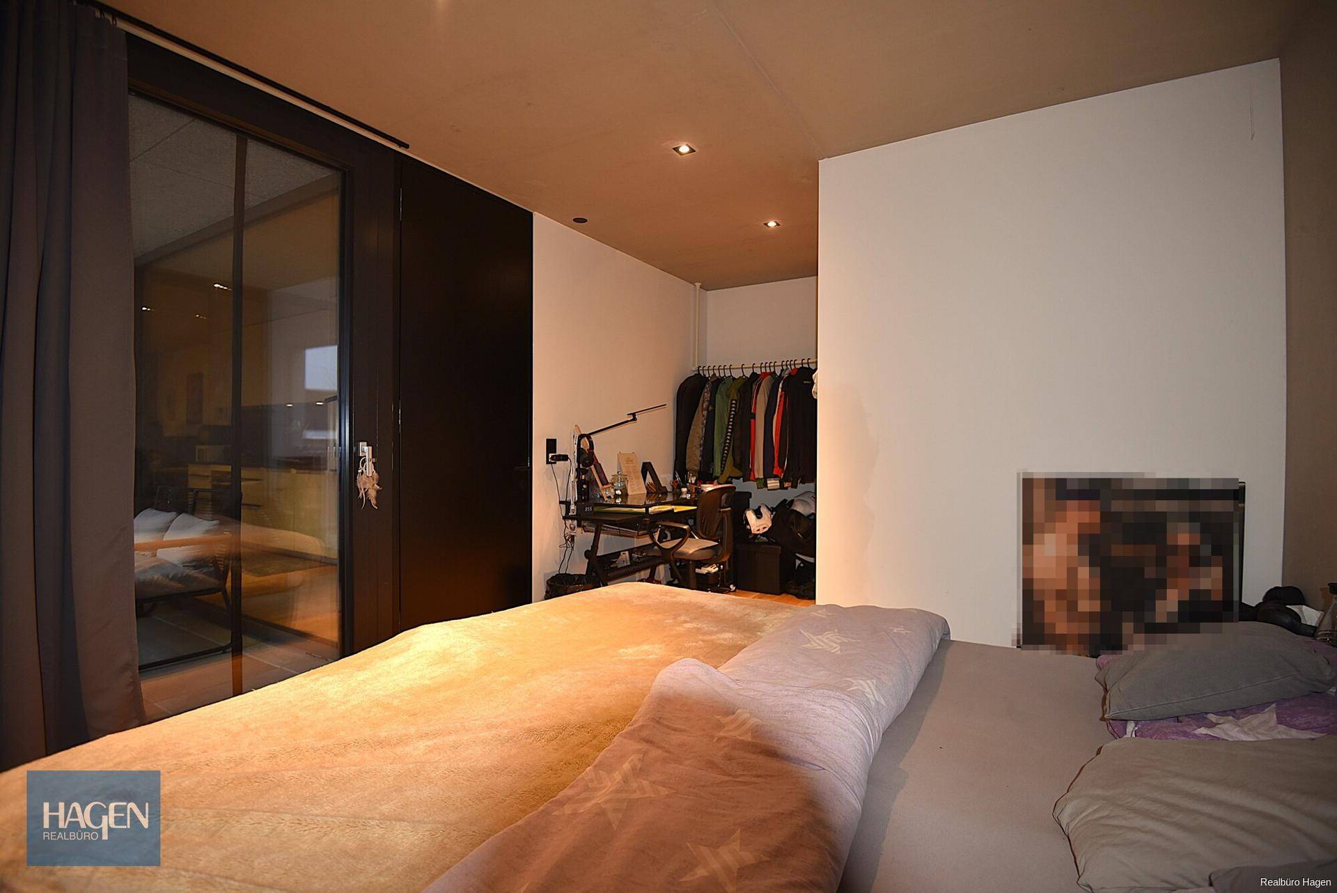 Schlafzimmer mit Zugang zu einem Balkon durch große Glasfenster und Kleiderstange.