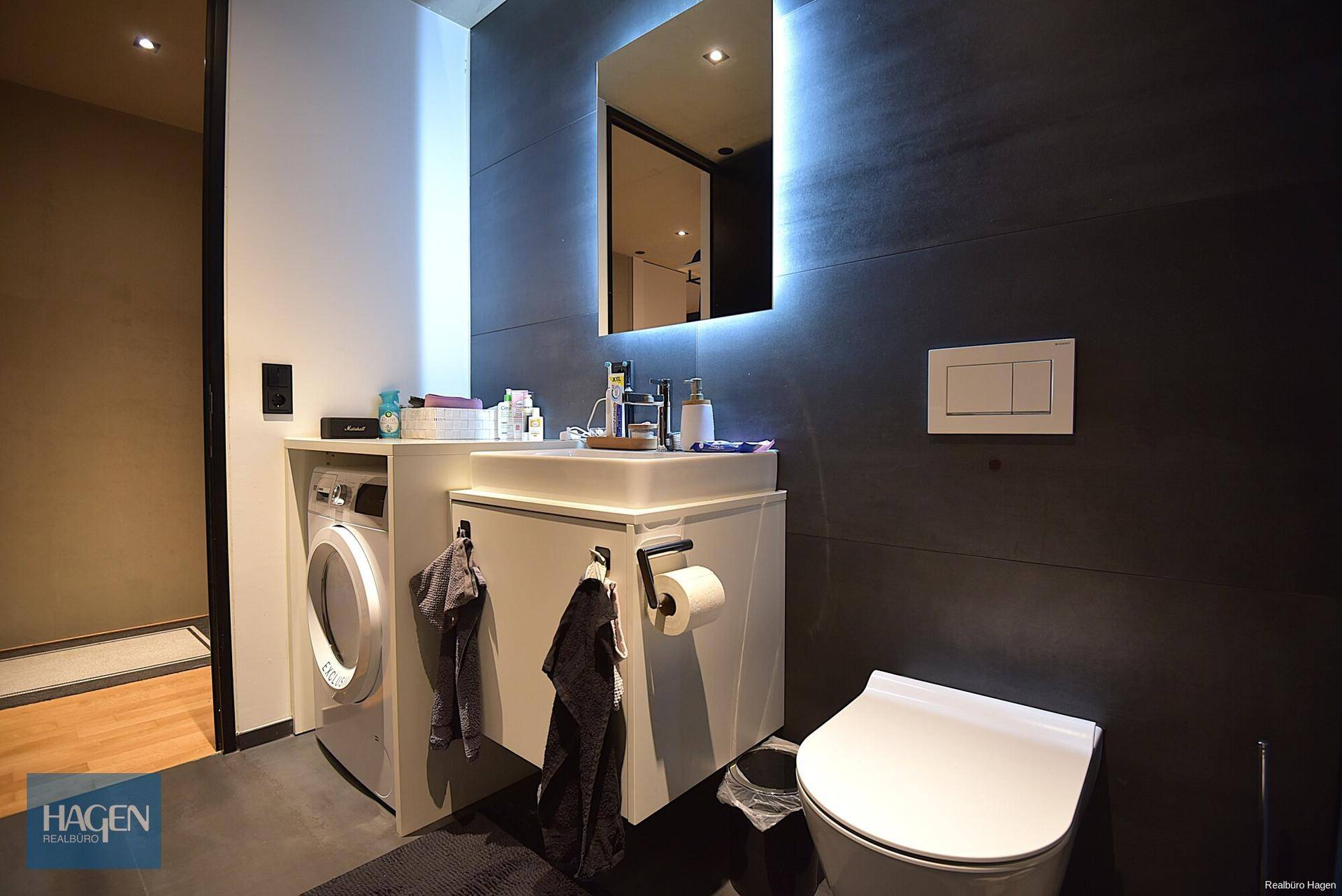 Zeitgemäßes Badezimmer mit Waschtisch, Toilette und integrierter Waschmaschine.