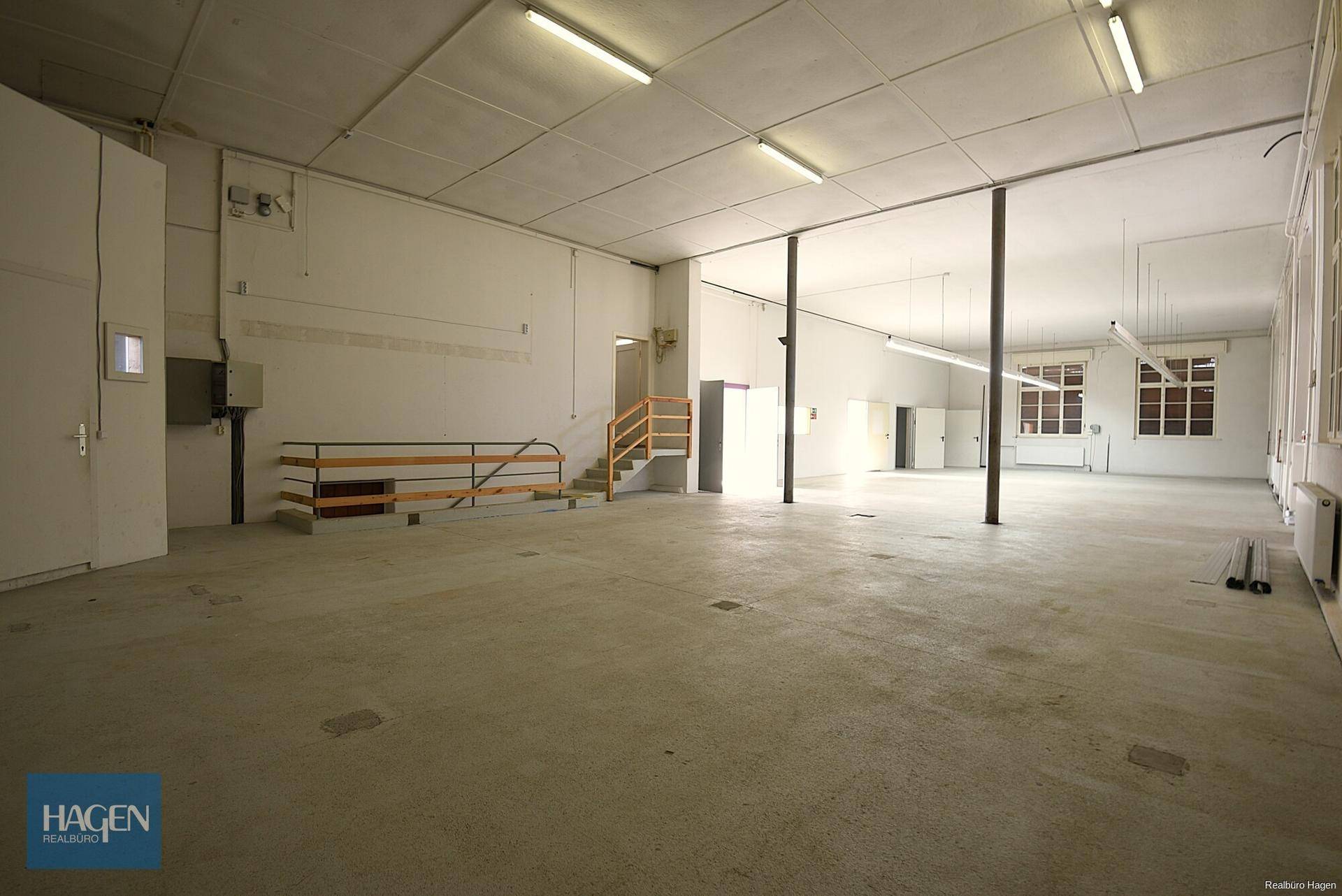 Großer, offener Industrieraum mit Betonboden, Stützen und einer Treppe.