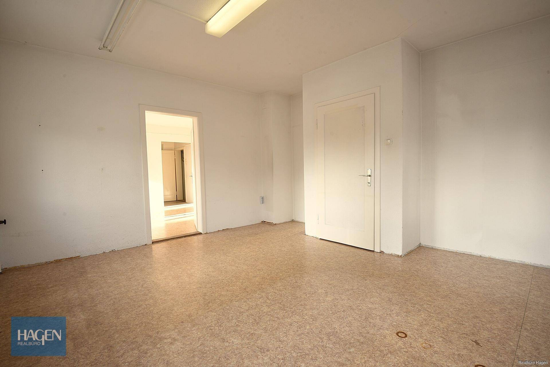 Heller Büroraum mit Linoleumboden und Zugang zu einem weiteren Raum.