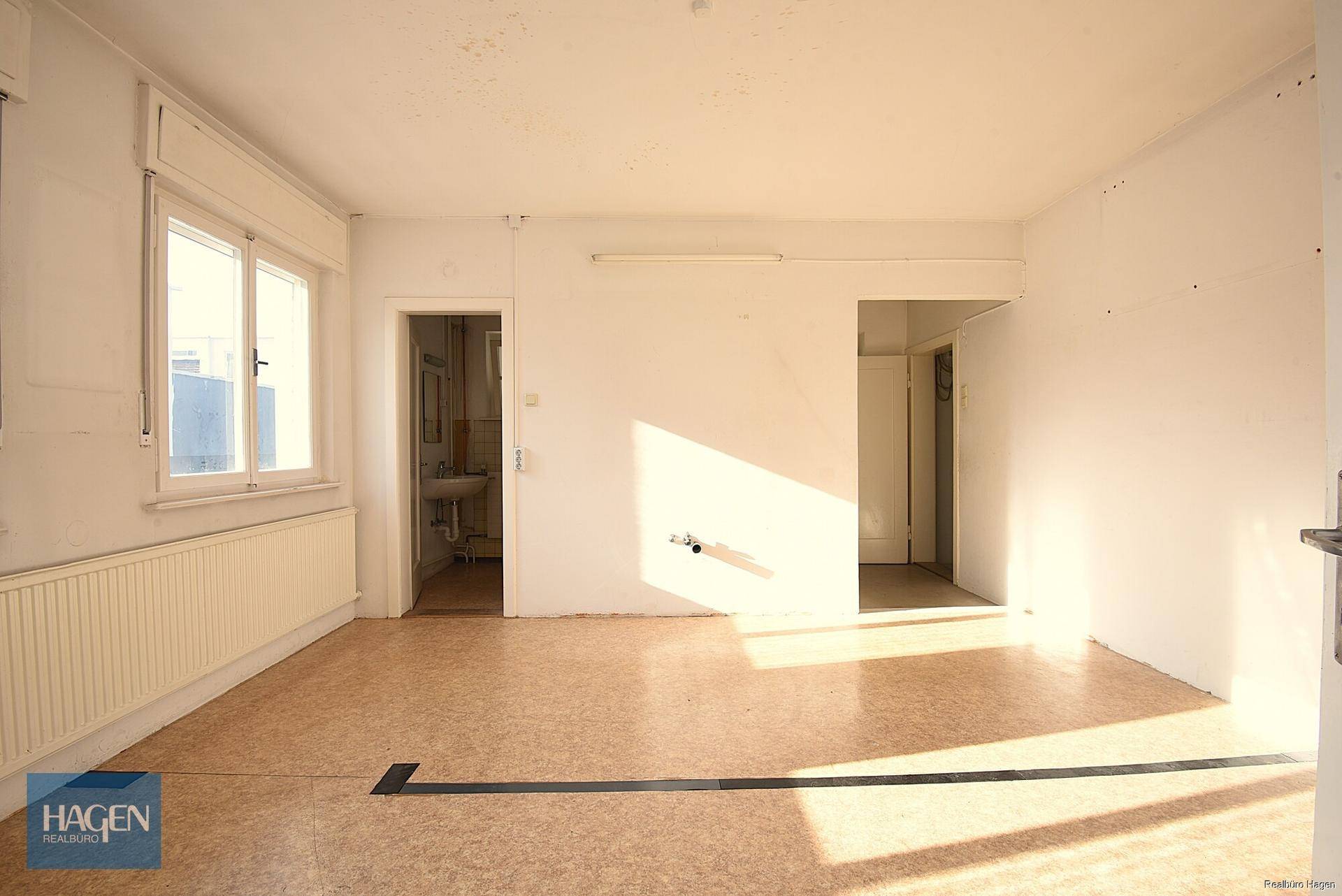 Heller Büroraum mit Linoleumboden und Blick in einen angrenzenden Raum.