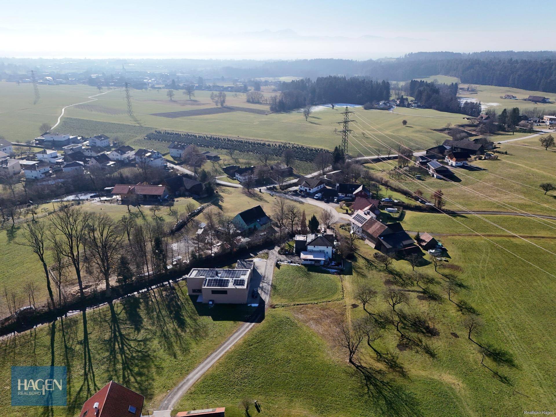 Weitläufige Luftaufnahme einer ländlichen Gegend mit Häusern, Feldern und Bergen im Hintergrund.