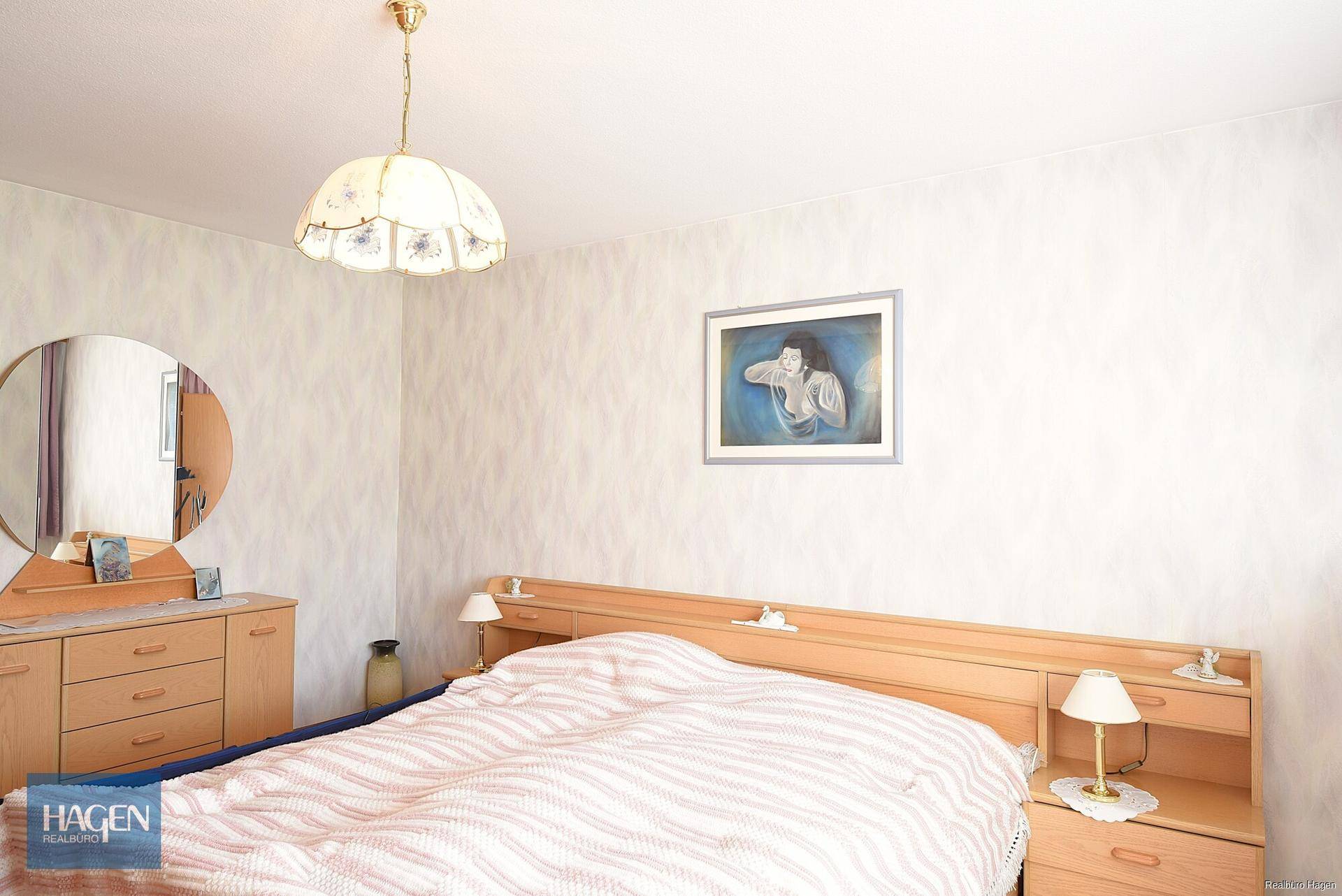 Schlafzimmer mit Doppelbett, Holzmöbeln und einem runden Spiegel über der Kommode.