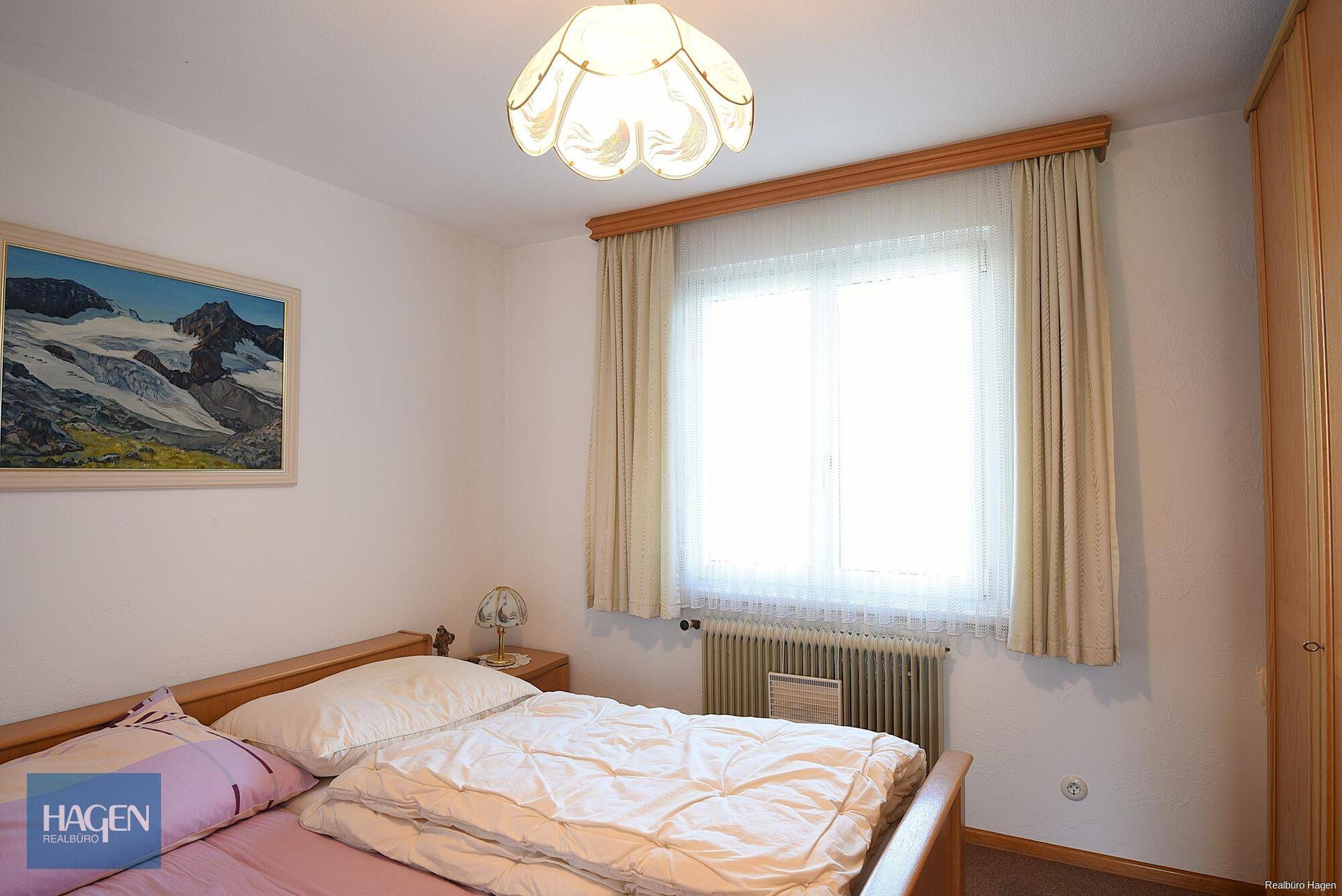 Helles Schlafzimmer mit Doppelbett, Holzmöbeln und Blick ins Grüne durch das Fenster.