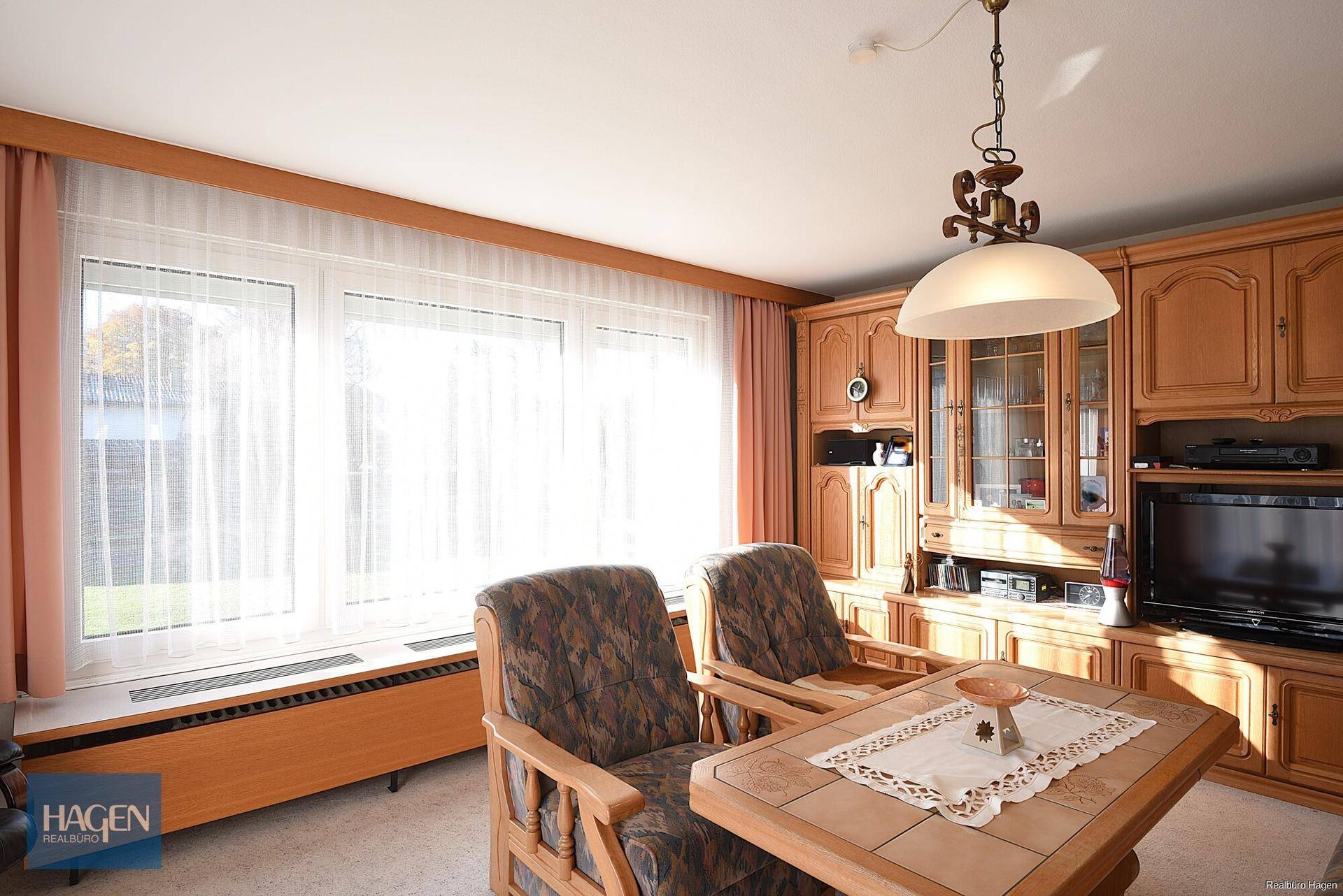 Gemütliches Wohnzimmer mit Holzmöbeln, großem Fenster und traditioneller Einrichtung.
