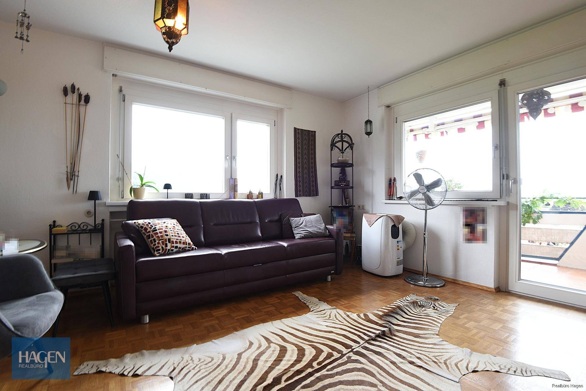 Gemütliches Wohnzimmer mit dunklem Sofa, Parkettboden und Zugang zu einem Außenbereich.