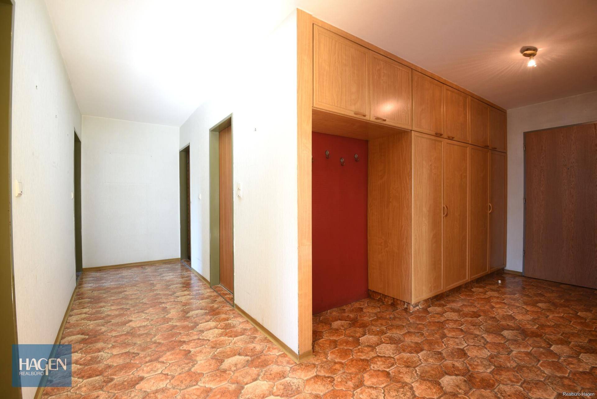 Flur mit gemusterten Fliesen, Einbauschränken und einer roten Akzentwand mit Garderobe.