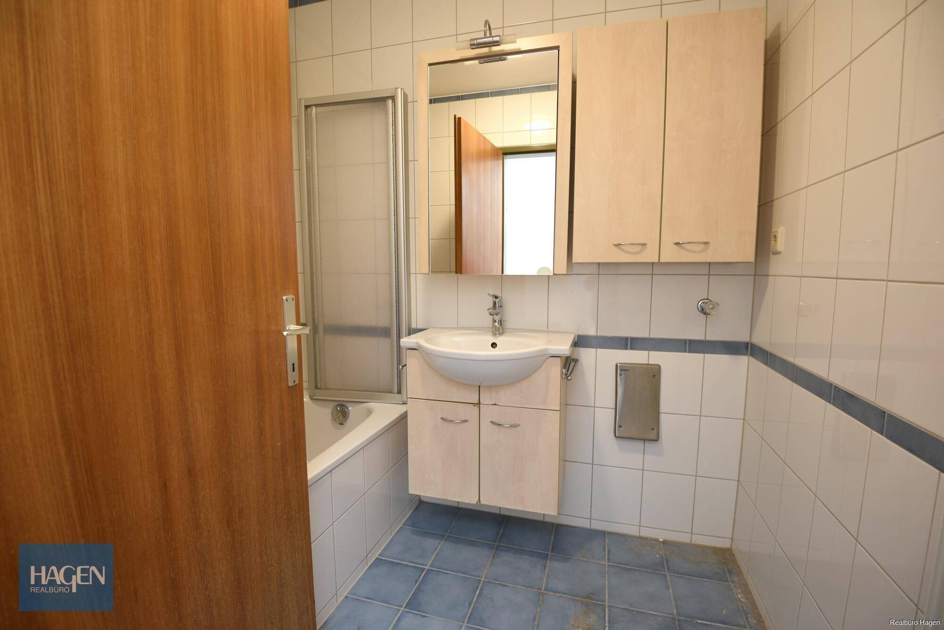 Badezimmer mit blauen und weißen Fliesen, Waschbecken, Spiegelschrank und Badewanne mit Duschwand.