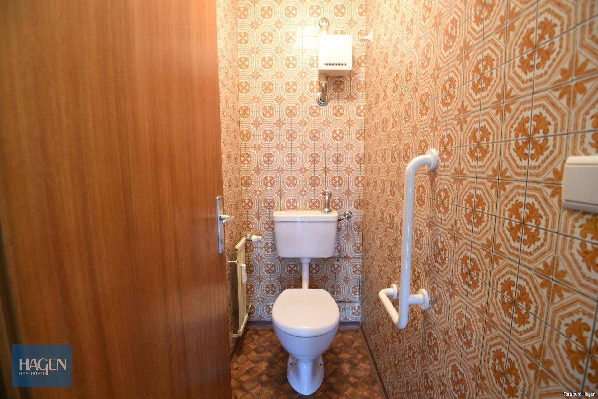 Separate Toilette mit gemusterten Fliesen, WC und Haltegriffen für zusätzliche Sicherheit.