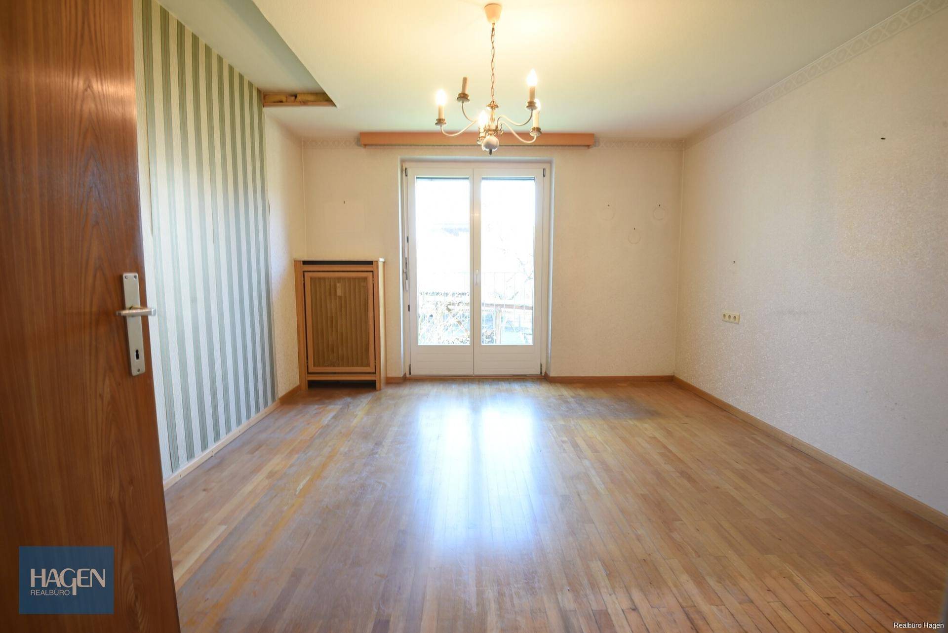 Heller Raum mit Laminatboden, Kronleuchter und Zugang zu einem französischen Balkon.